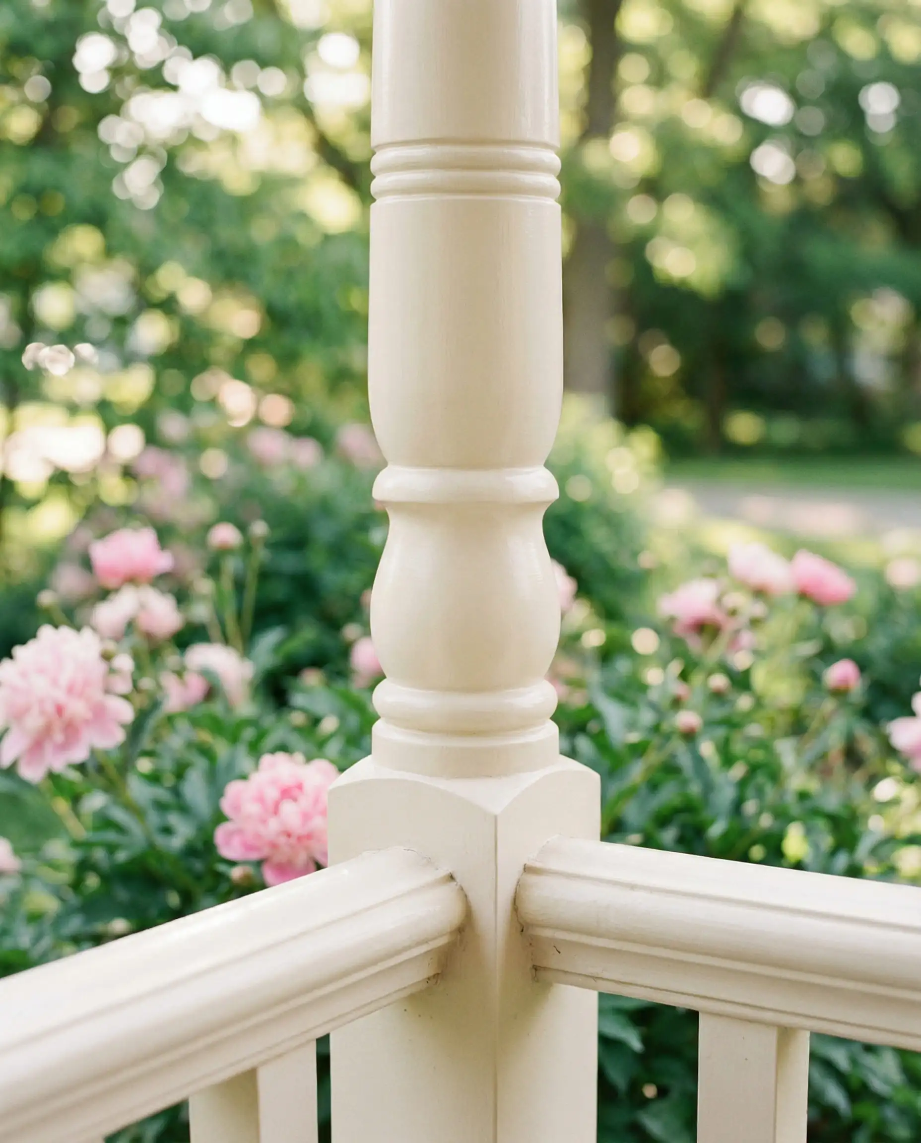 Macro shot of a turned wood porch column painted in Behr Swiss Coffee semi-gloss, showing the creamy yellow undertones against a garden background.