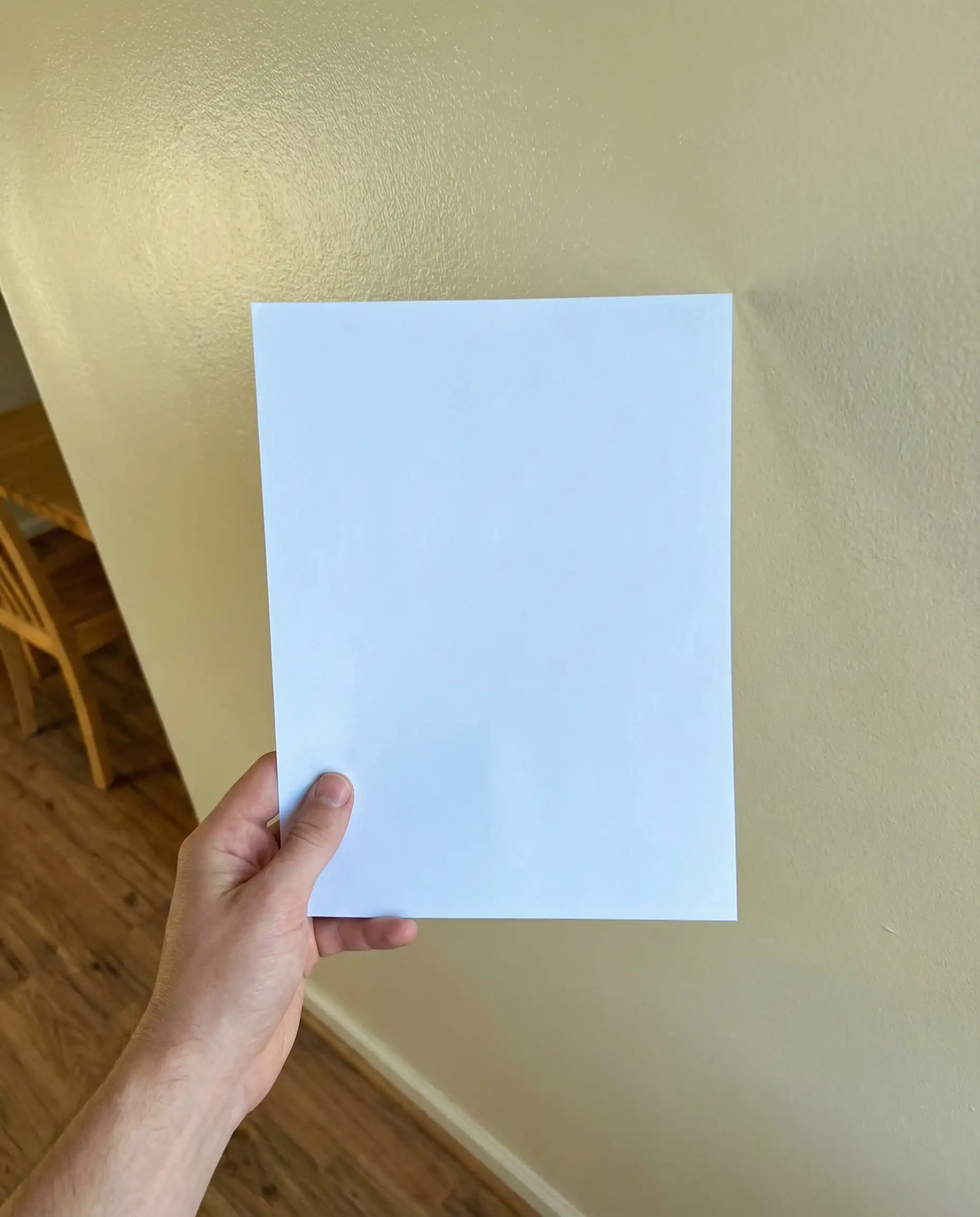 Hand holding a white sheet of paper against a Benjamin Moore Swiss Coffee wall to reveal the creamy undertone.