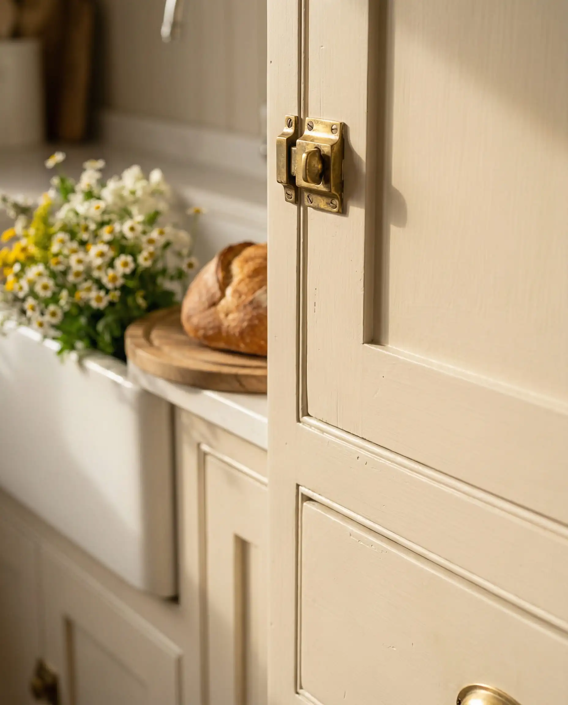 Macro detail of a cream painted cabinet door with an unlacquered brass latch catching the light.