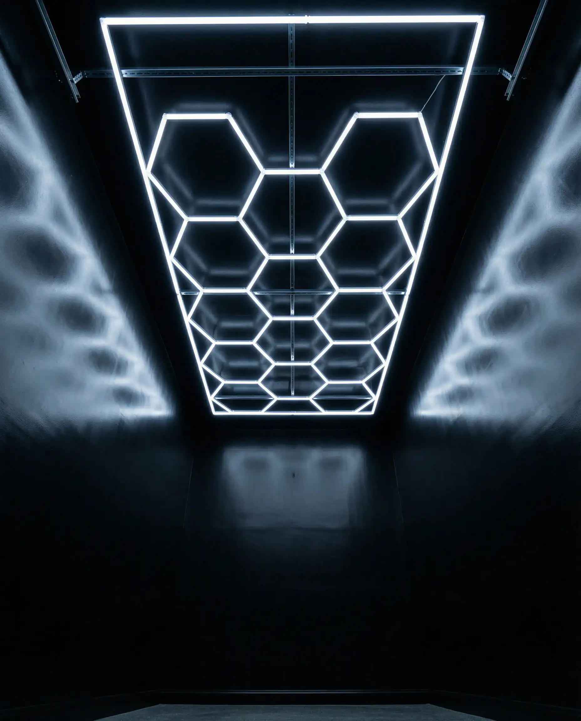 Dark grey garage walls illuminated by a modern hexagonal LED ceiling light grid, demonstrating proper lighting for dark interiors.