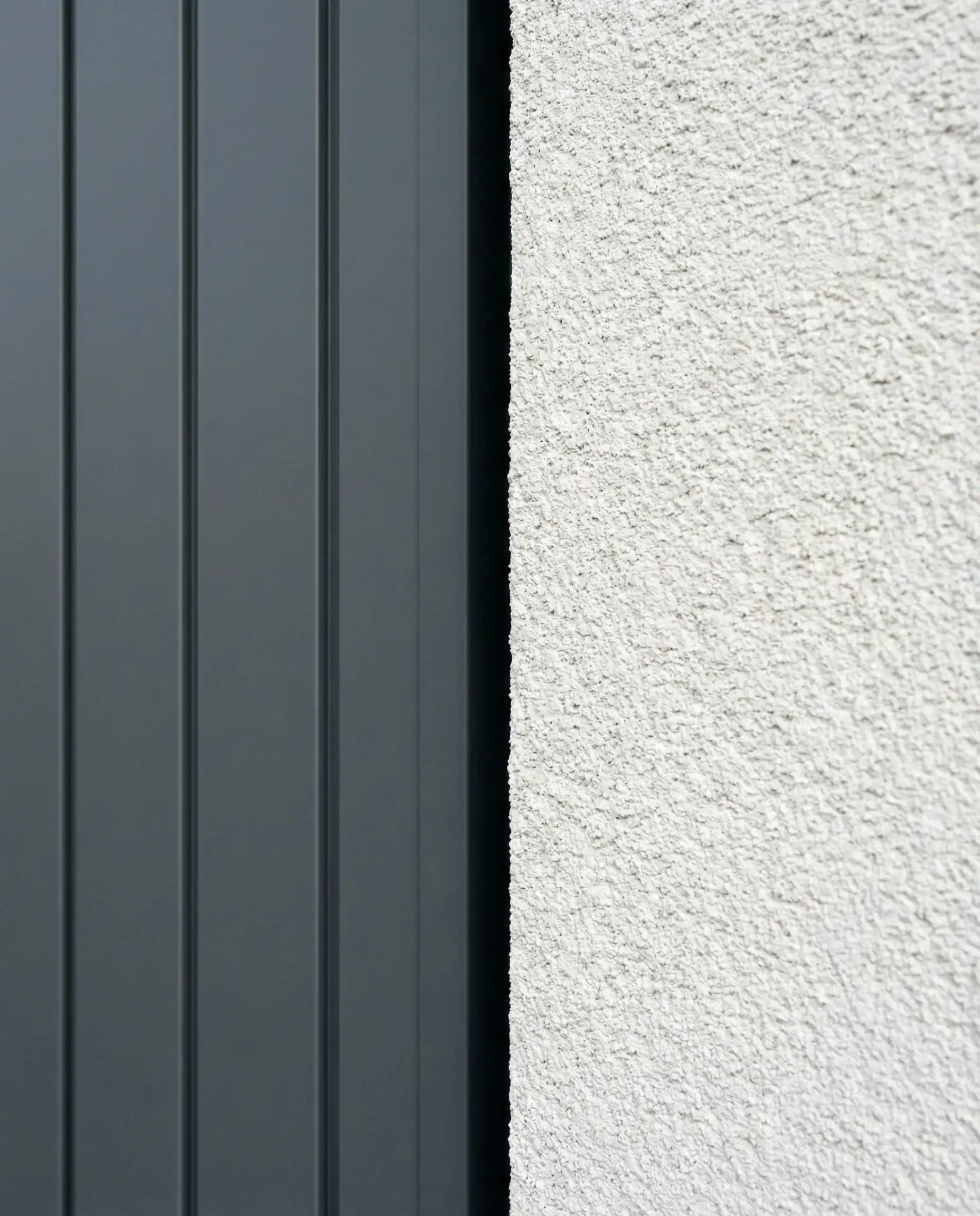 Macro architectural detail showing the sharp contrast and junction between smooth graphite gray vertical siding and rough white stucco texture.