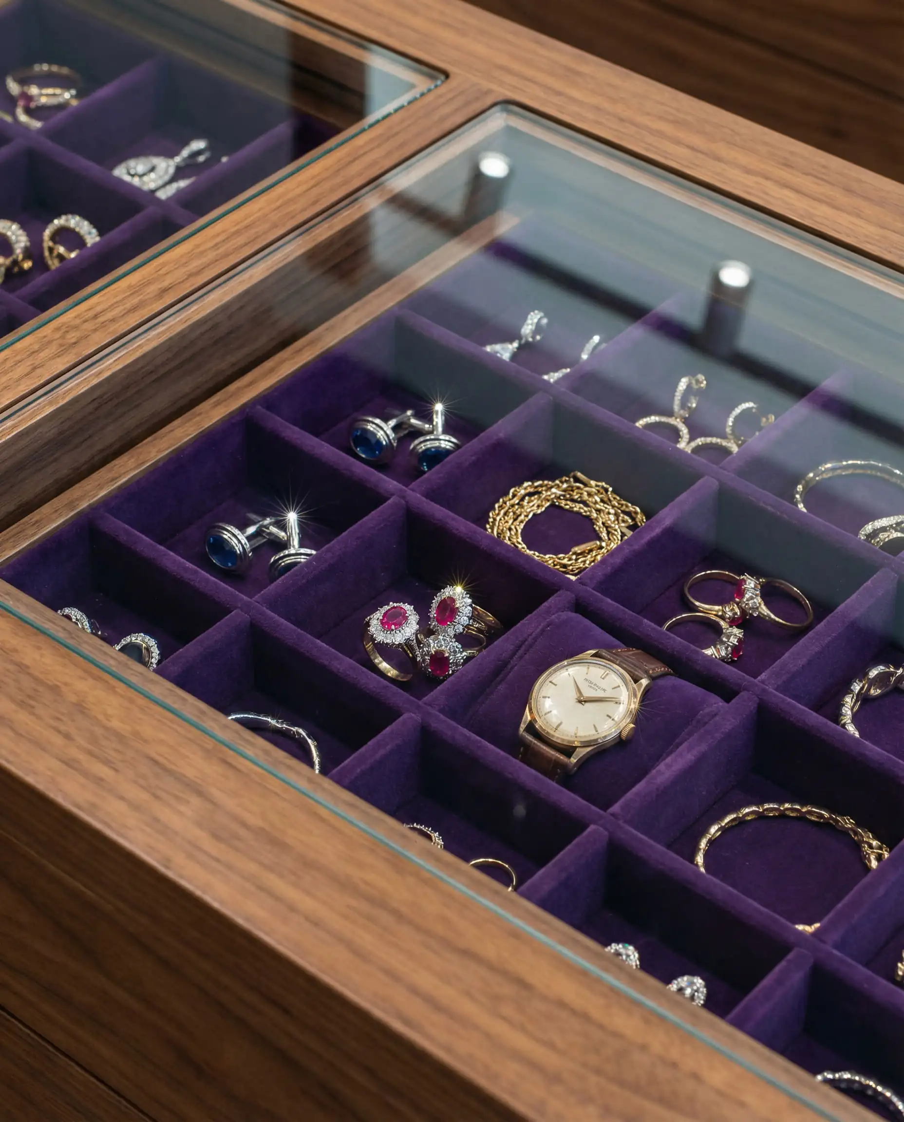 Macro shot of a glass-topped drawer showing rings and necklaces organized on grey velvet lining.