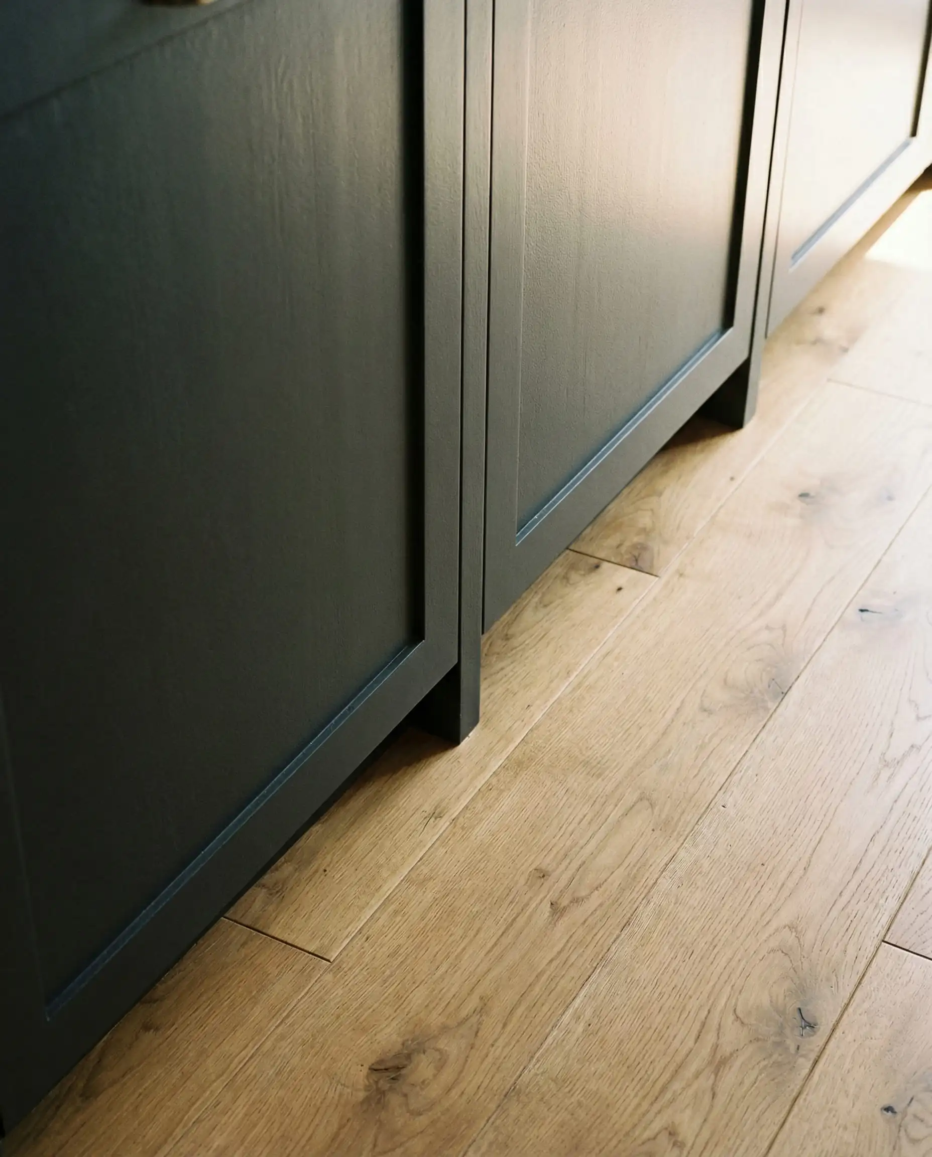 Top down view of Sherwin-Williams Iron Ore cabinets meeting wide plank white oak flooring.