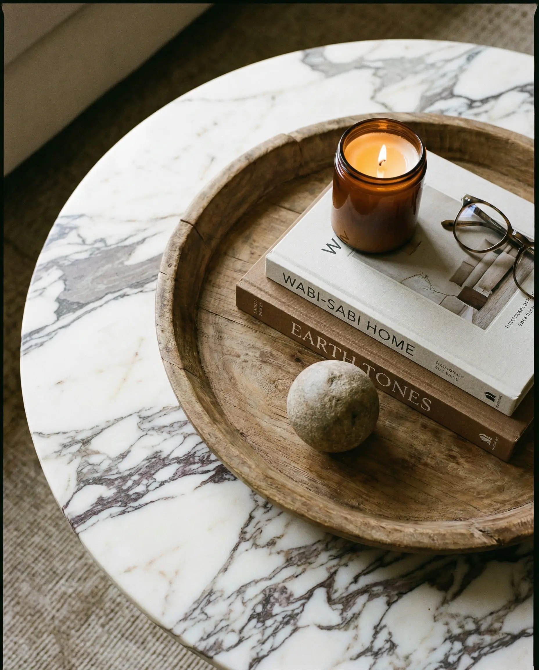 Round marble coffee table styled with design books, tray, and candle.