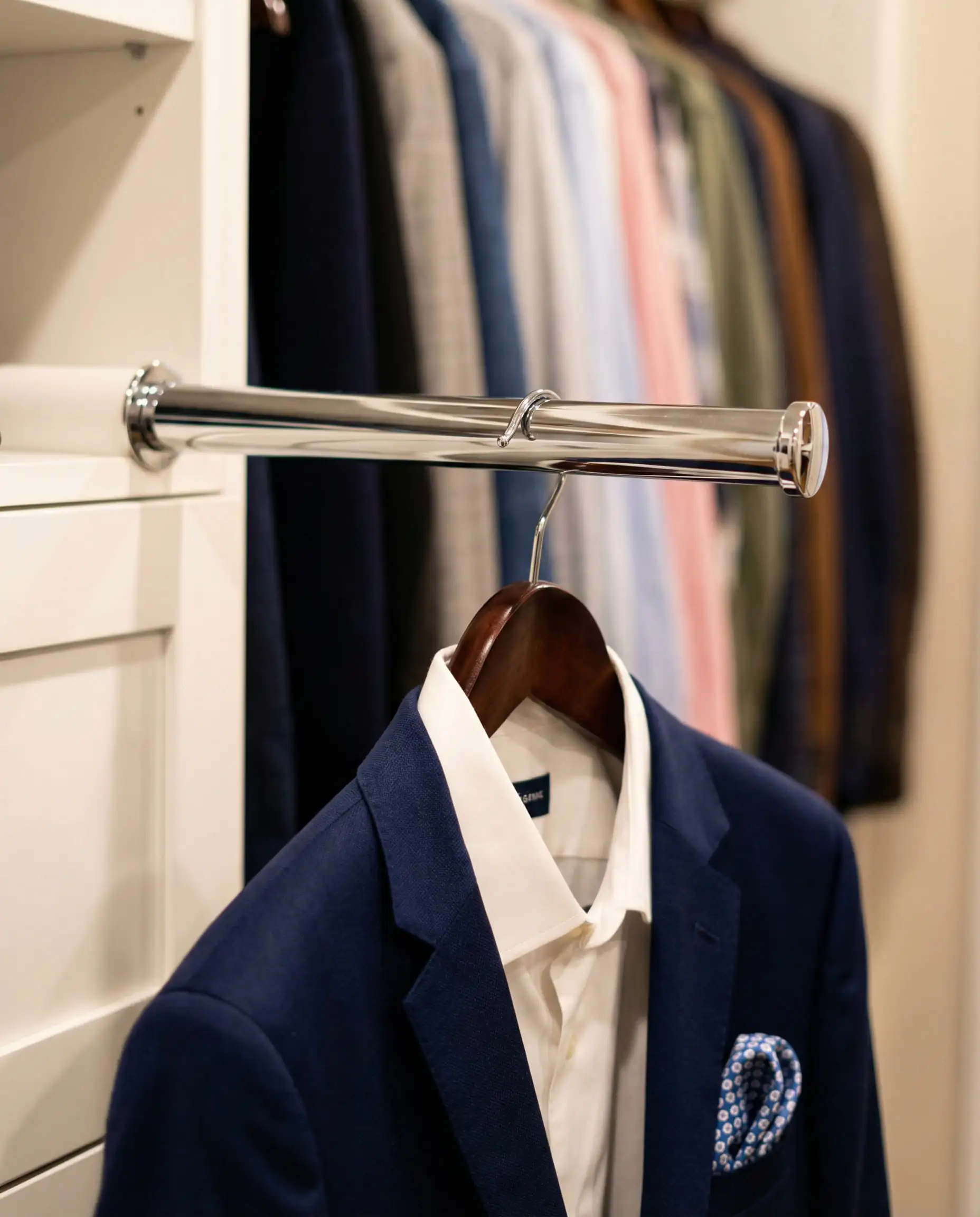 Retractable chrome valet rod pulled out holding a navy blazer against a blurred background.