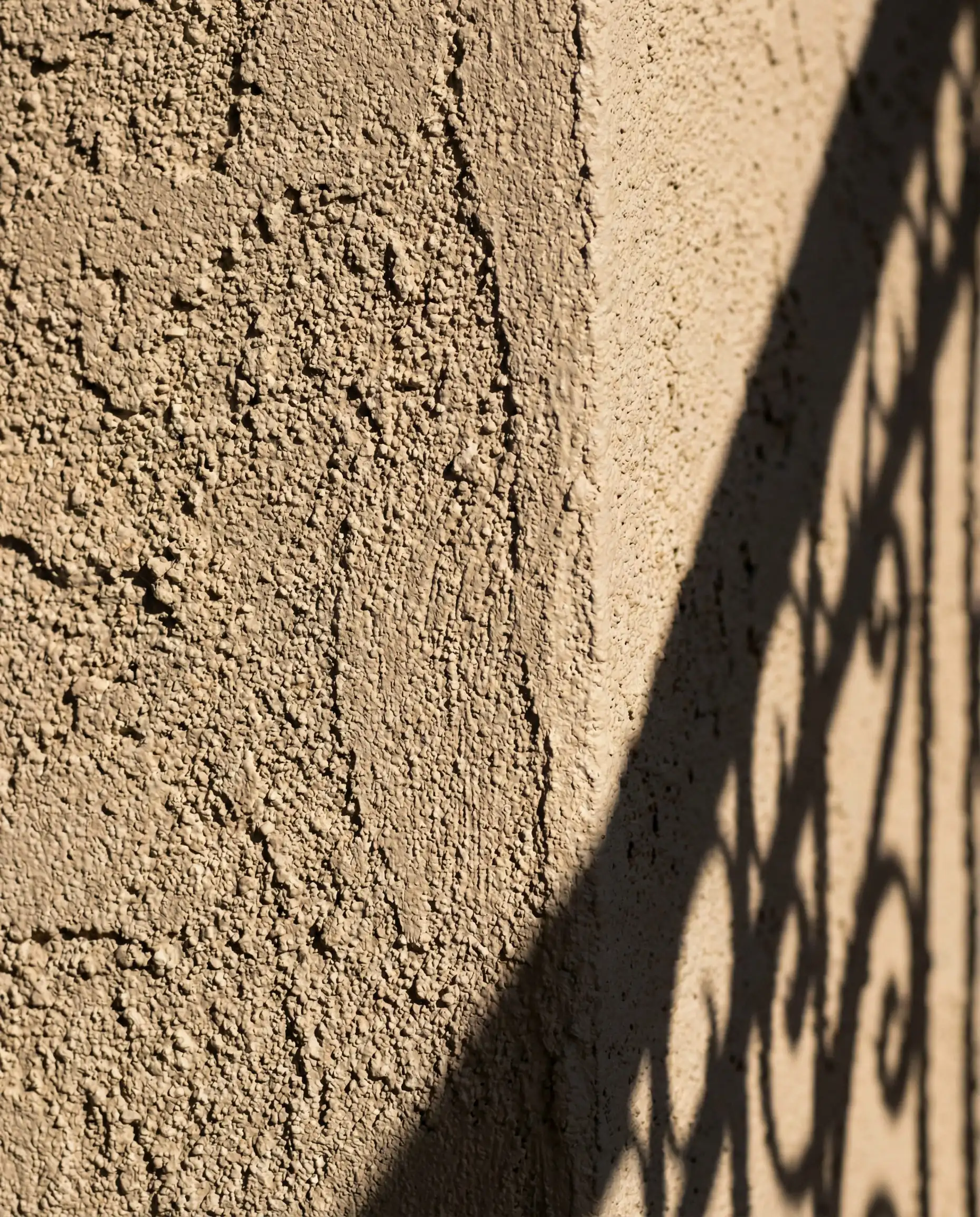 Close-up of rough stucco texture painted in Sherwin-Williams Accessible Beige in bright sunlight.