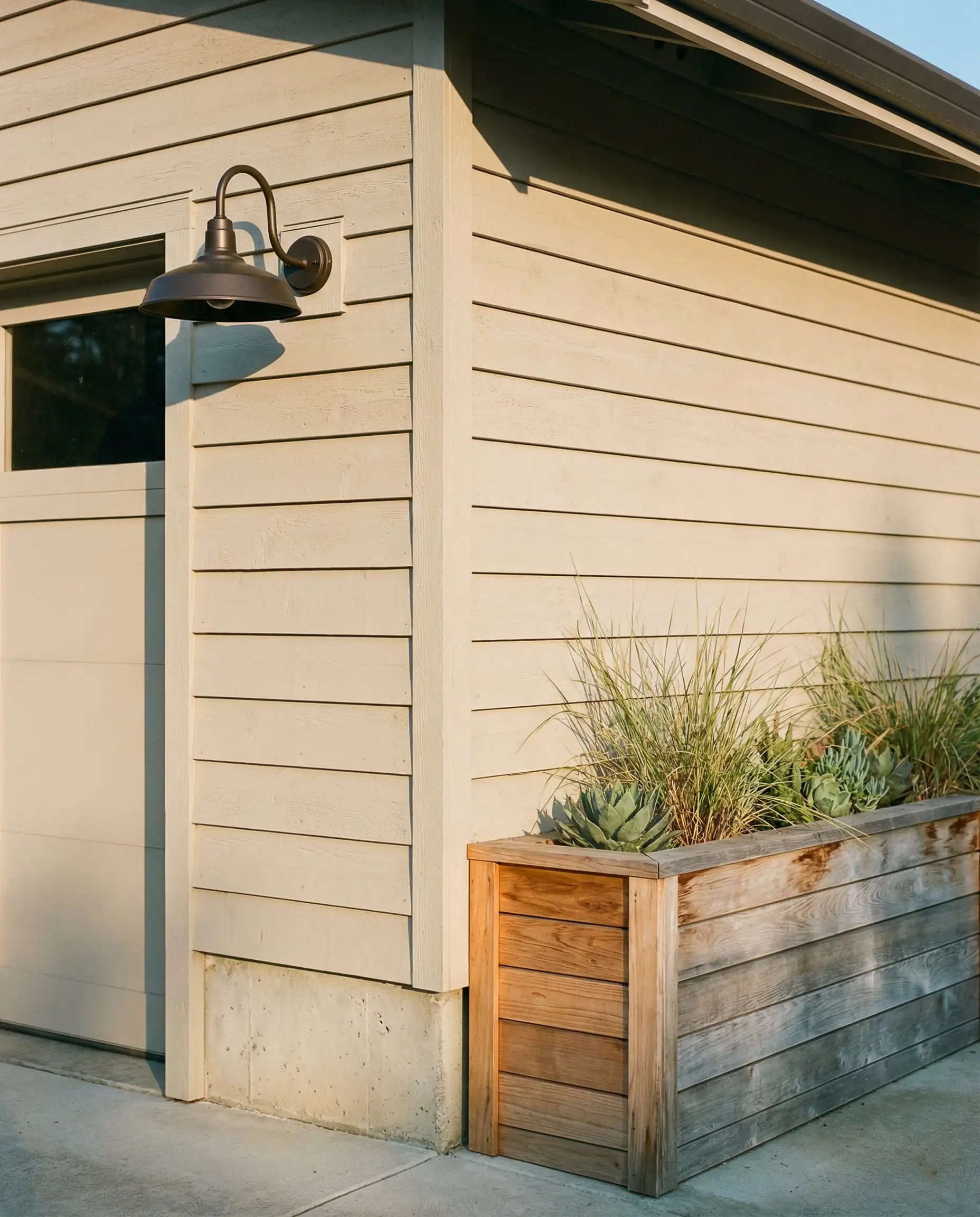 Exterior garage detail showing Sherwin-Williams Natural Linen siding next to weathered cedar wood planter.