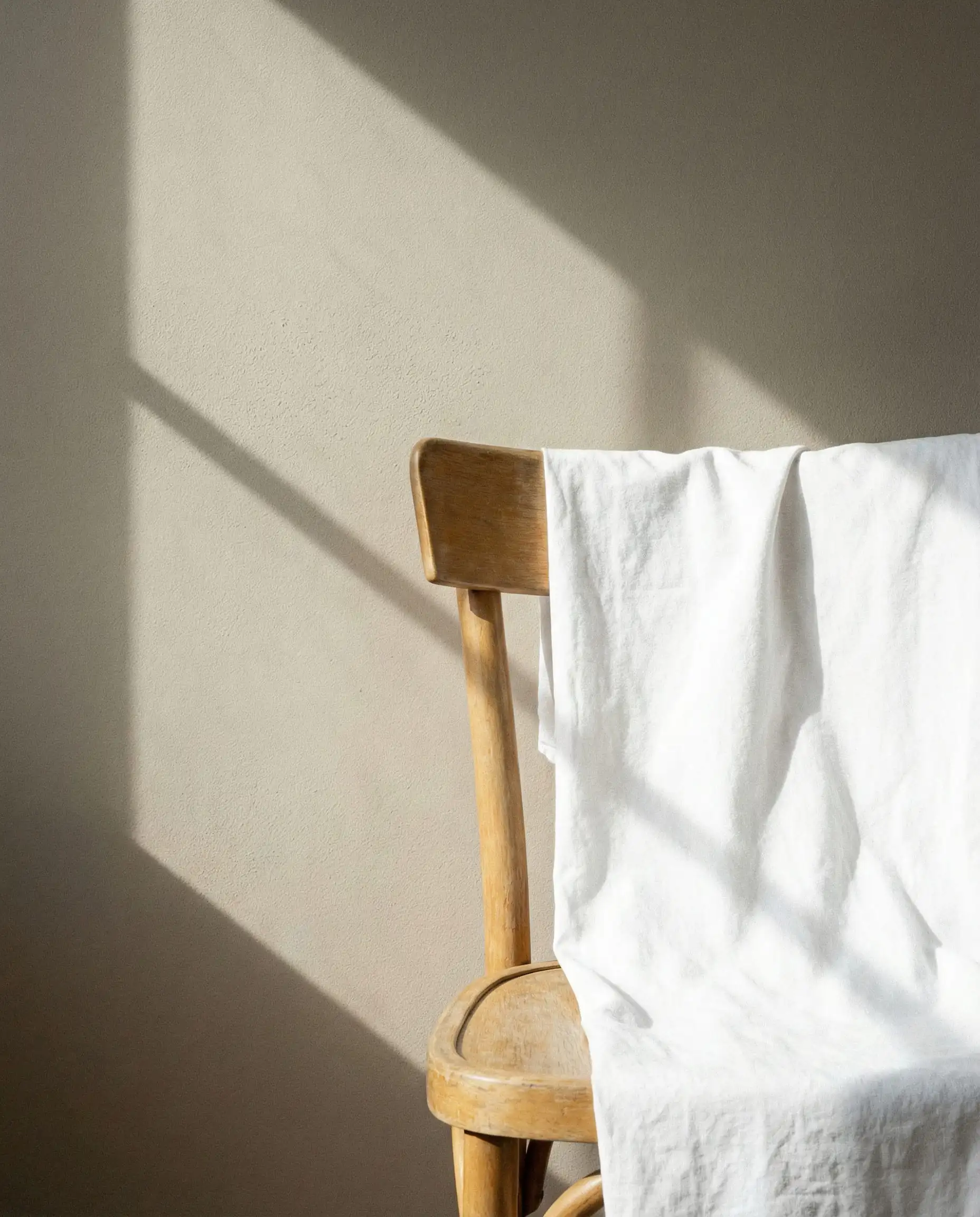 Detail shot of a white sheet draped over a chair against a Sherwin-Williams Shoji White wall to show the greige undertone.