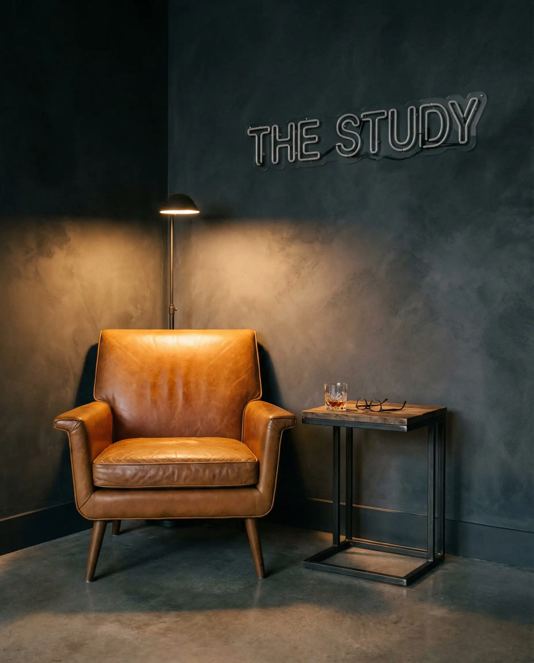 Garage converted into a lounge with soft charcoal walls, a cognac leather armchair, and a neon sign.