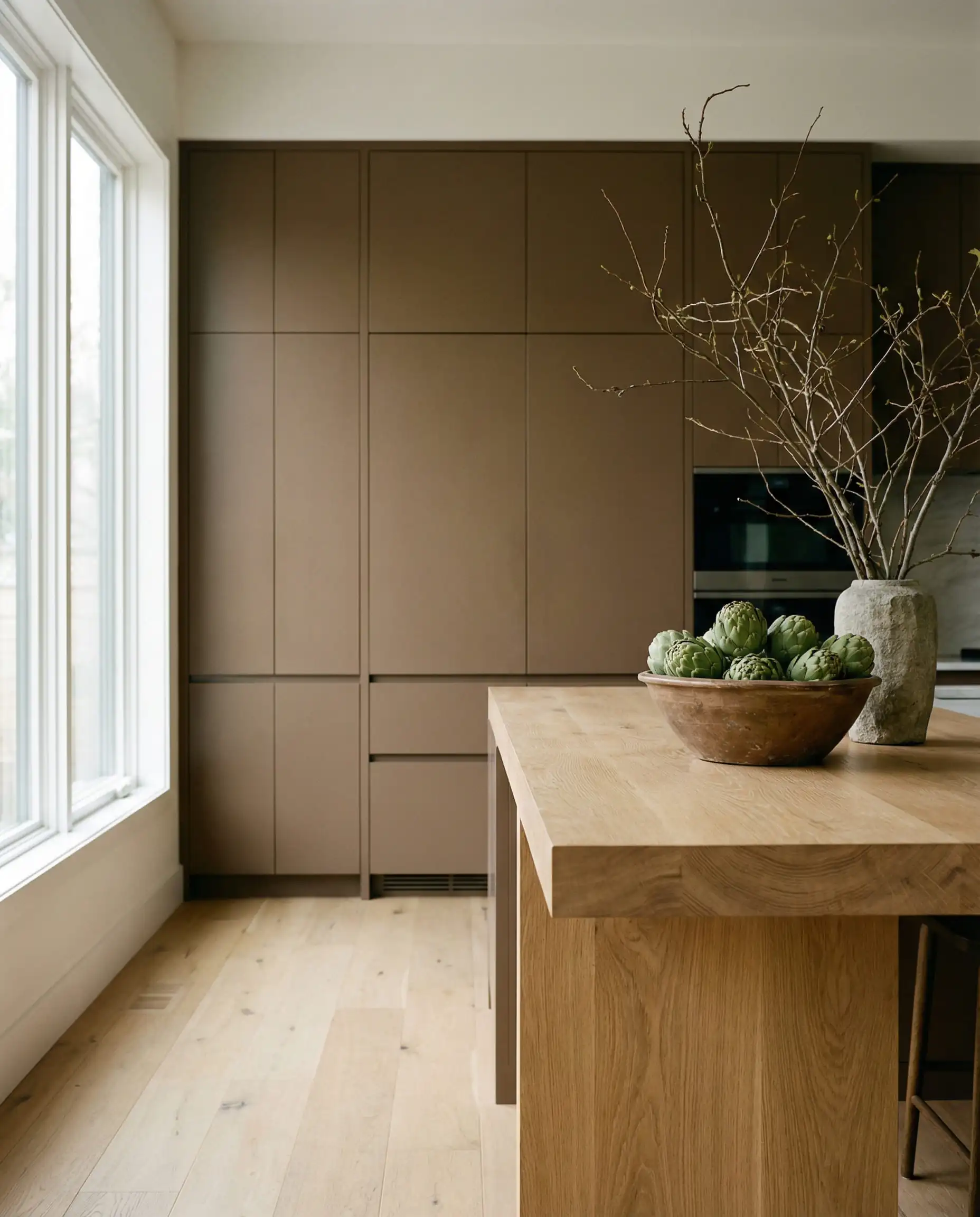 Vertical shot of floor-to-ceiling kitchen cabinets painted in Sherwin-Williams Universal Khaki SW 6150 next to a white oak island.