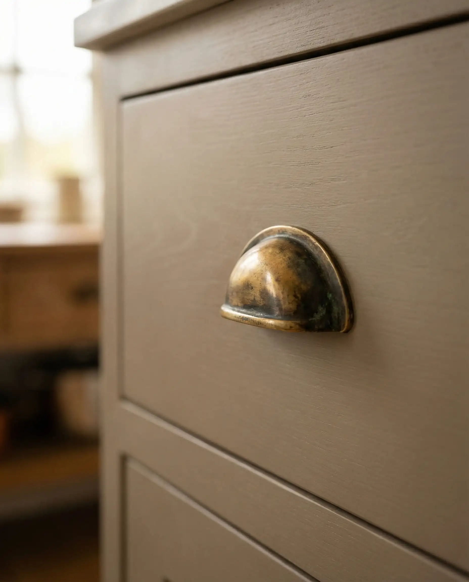 Macro shot of unlacquered brass cup pull on a drawer painted in Sherwin-Williams Universal Khaki showing patina.