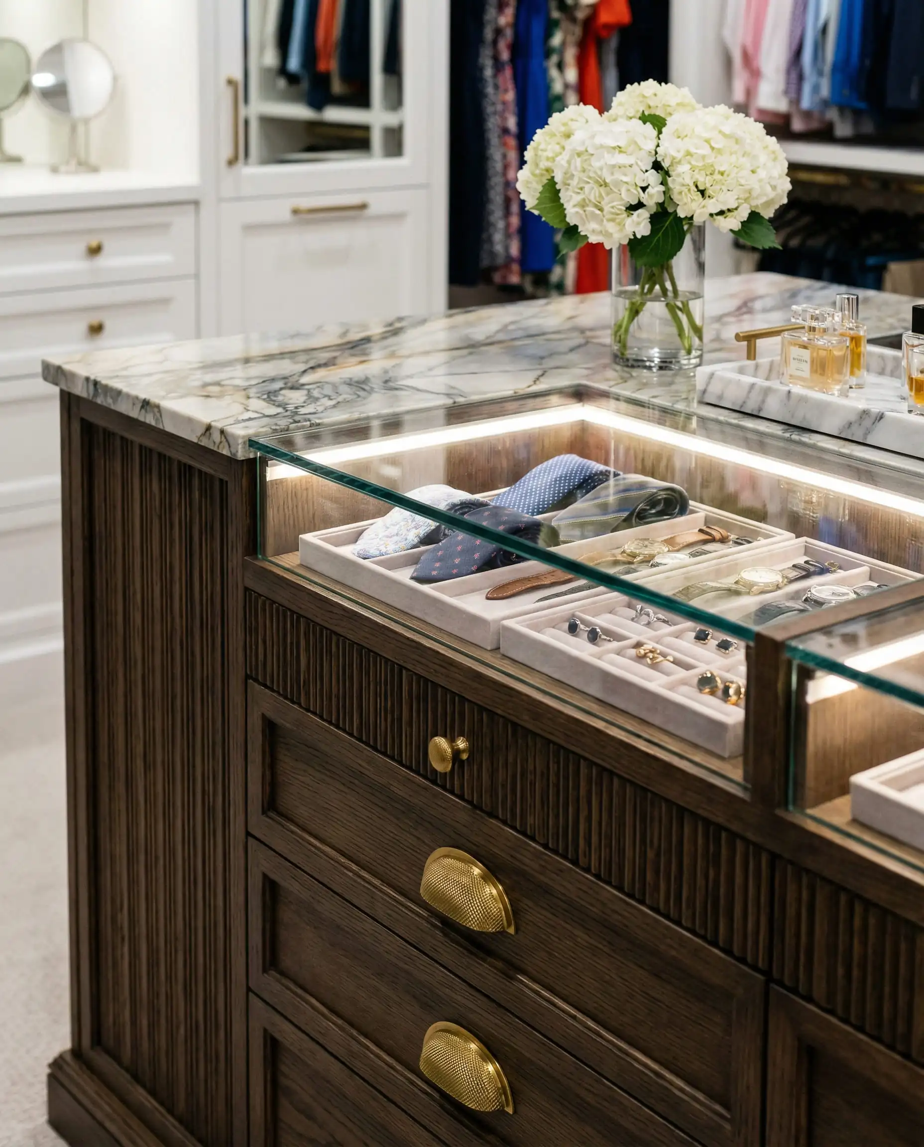 Close-up of a dark oak closet island with glass-top jewelry drawers and brass hardware.