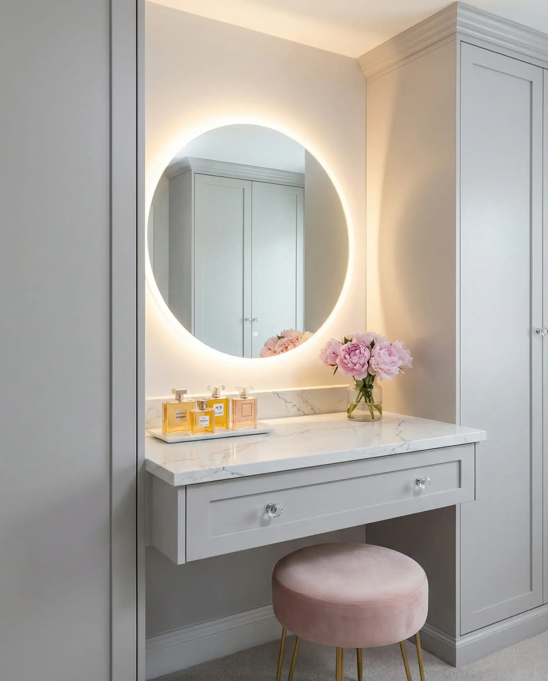 Built-in makeup vanity station inside a closet with a backlit round mirror and velvet stool.