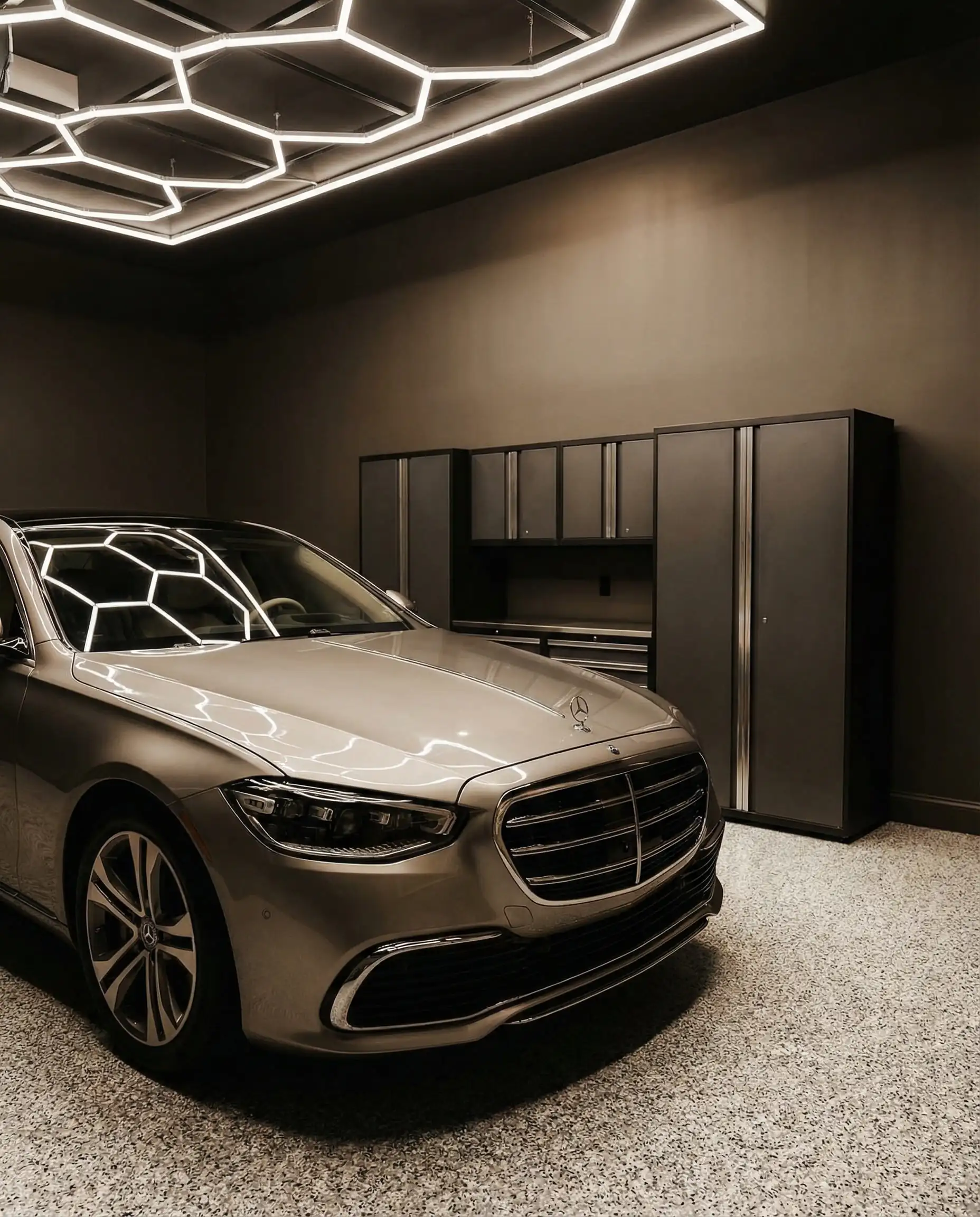 Modern garage interior with warm greige walls and epoxy flooring, featuring a silver luxury sedan and dark grey storage cabinets.
