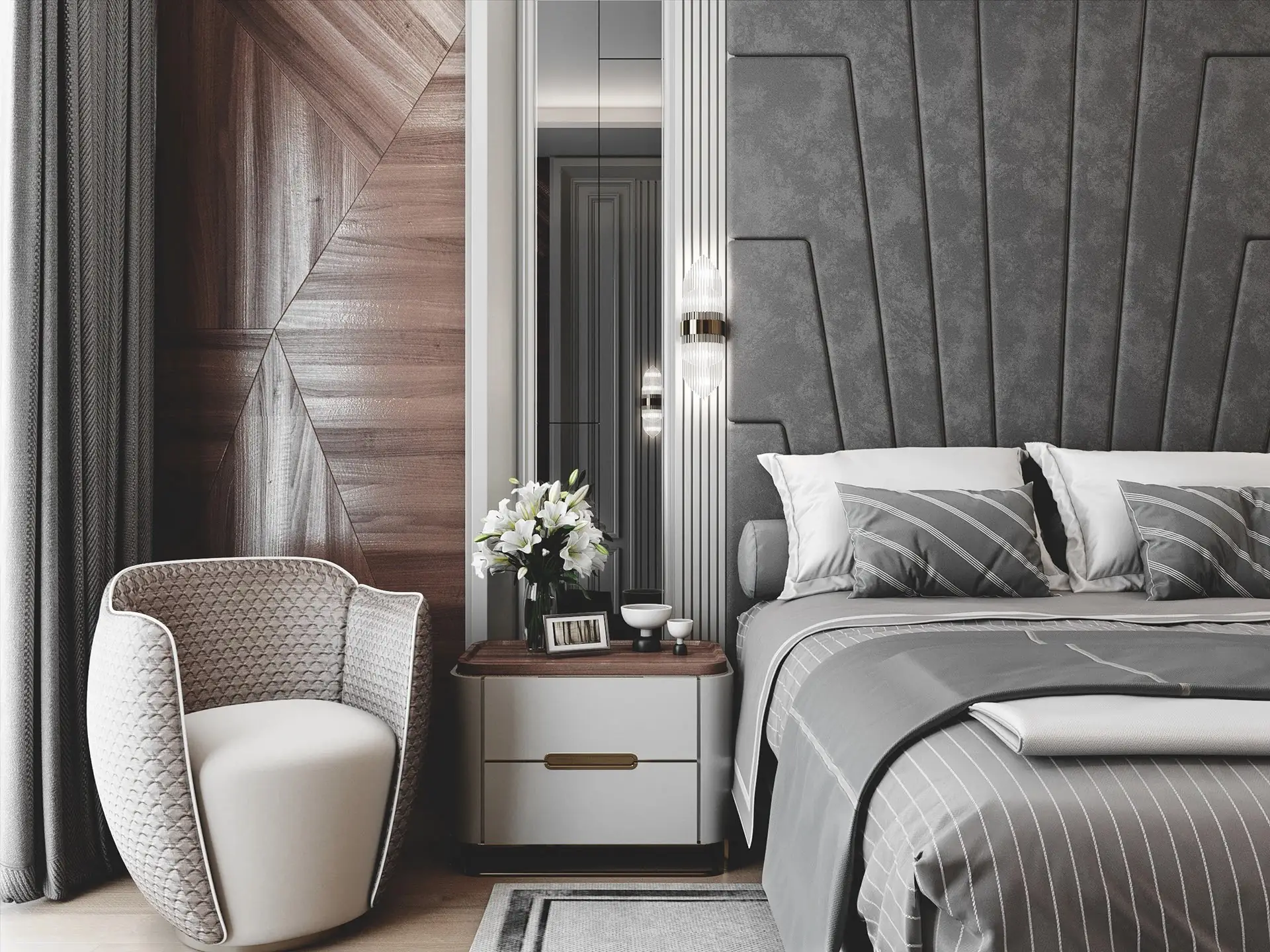 A close-up of a glamorous bedroom featuring a tall grey paneled headboard, a white nightstand, a sparkling glass wall sconce mounted on a mirrored panel, and a chic curved side chair against a geometric wood wall.