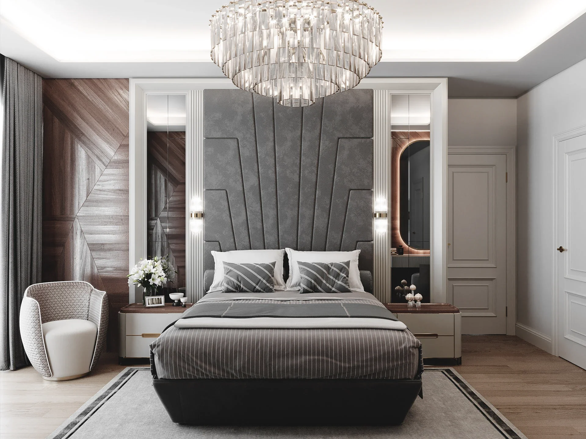 A glamorous bedroom centered around a very tall grey upholstered headboard, flanked by vertical mirrors and glass sconces, with a large crystal chandelier hanging above the bed.