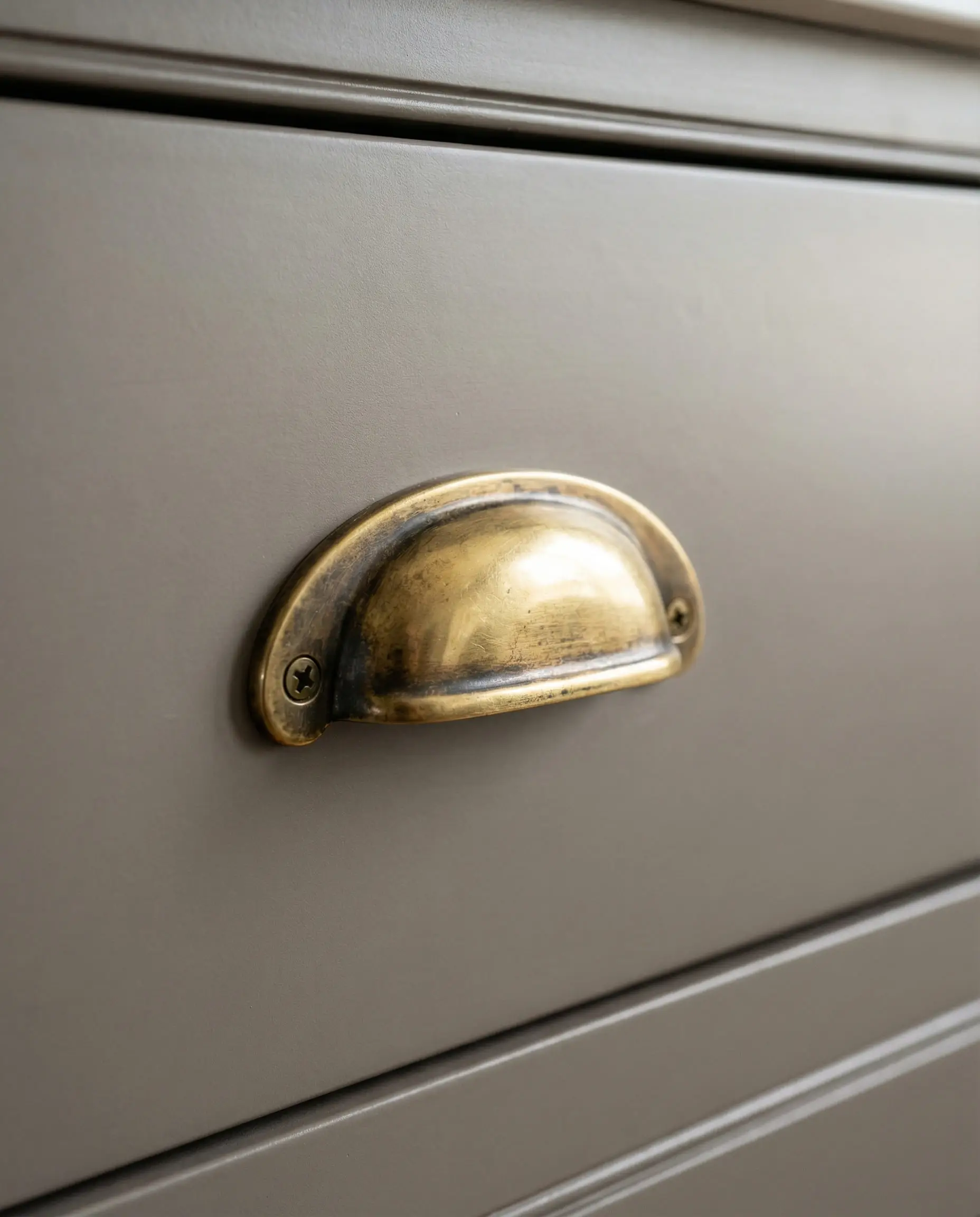 Macro shot of an unlacquered brass bin pull with patina on a satin gray drawer front.