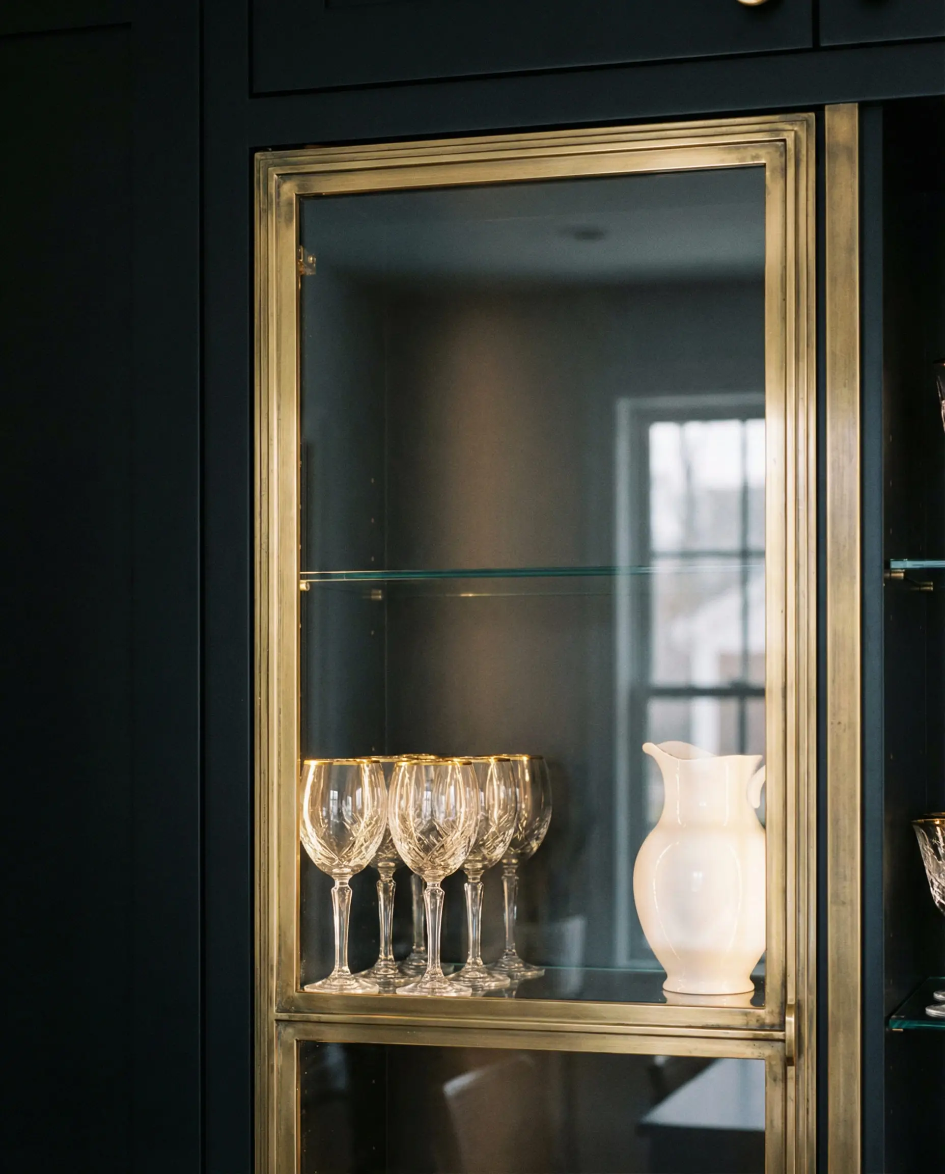 Close-up of a glass cabinet door with an antique brass frame and black interior, displaying crystal glassware.