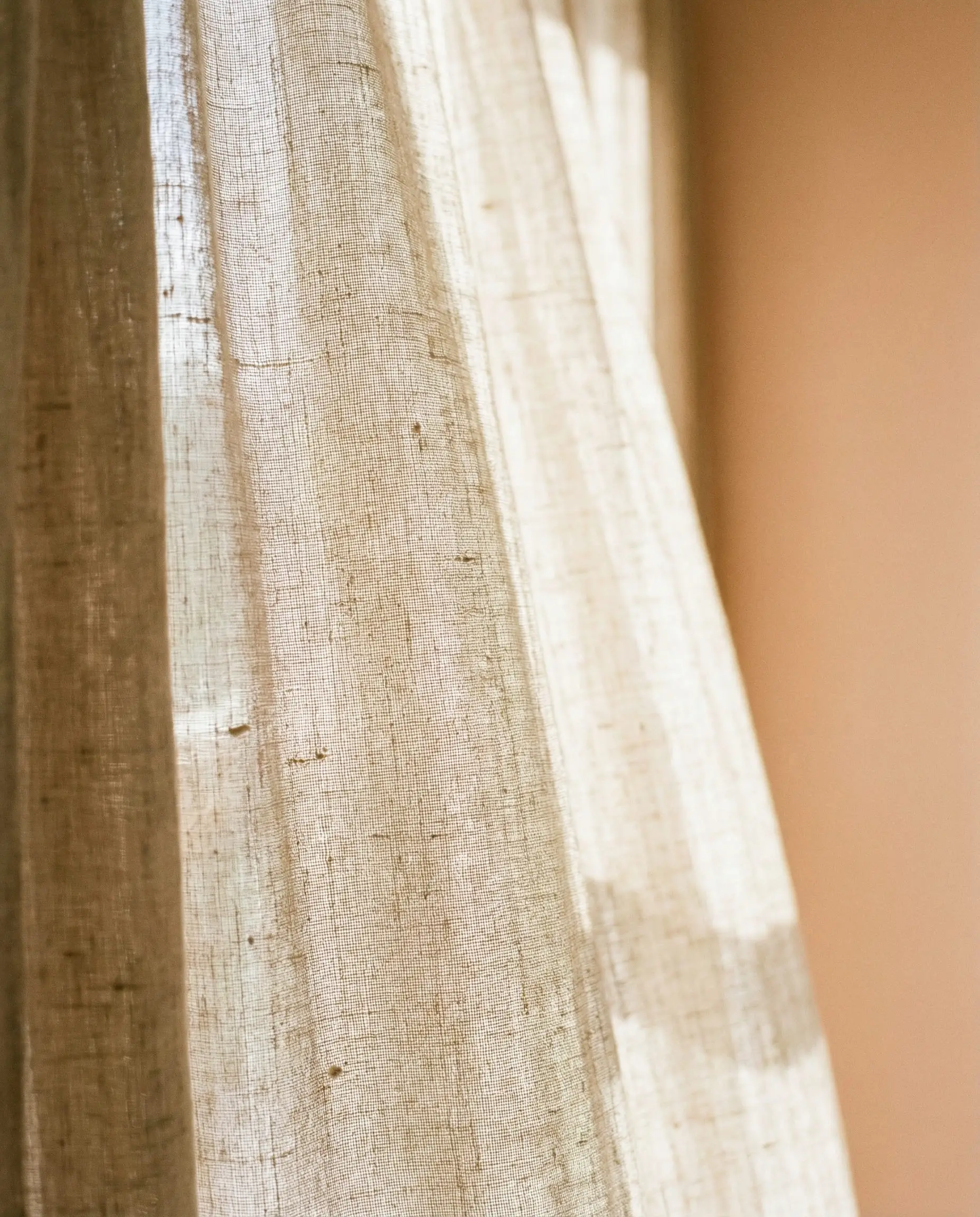 Close-up of beige linen curtains with visible weave texture hanging against a soft peach wall.
