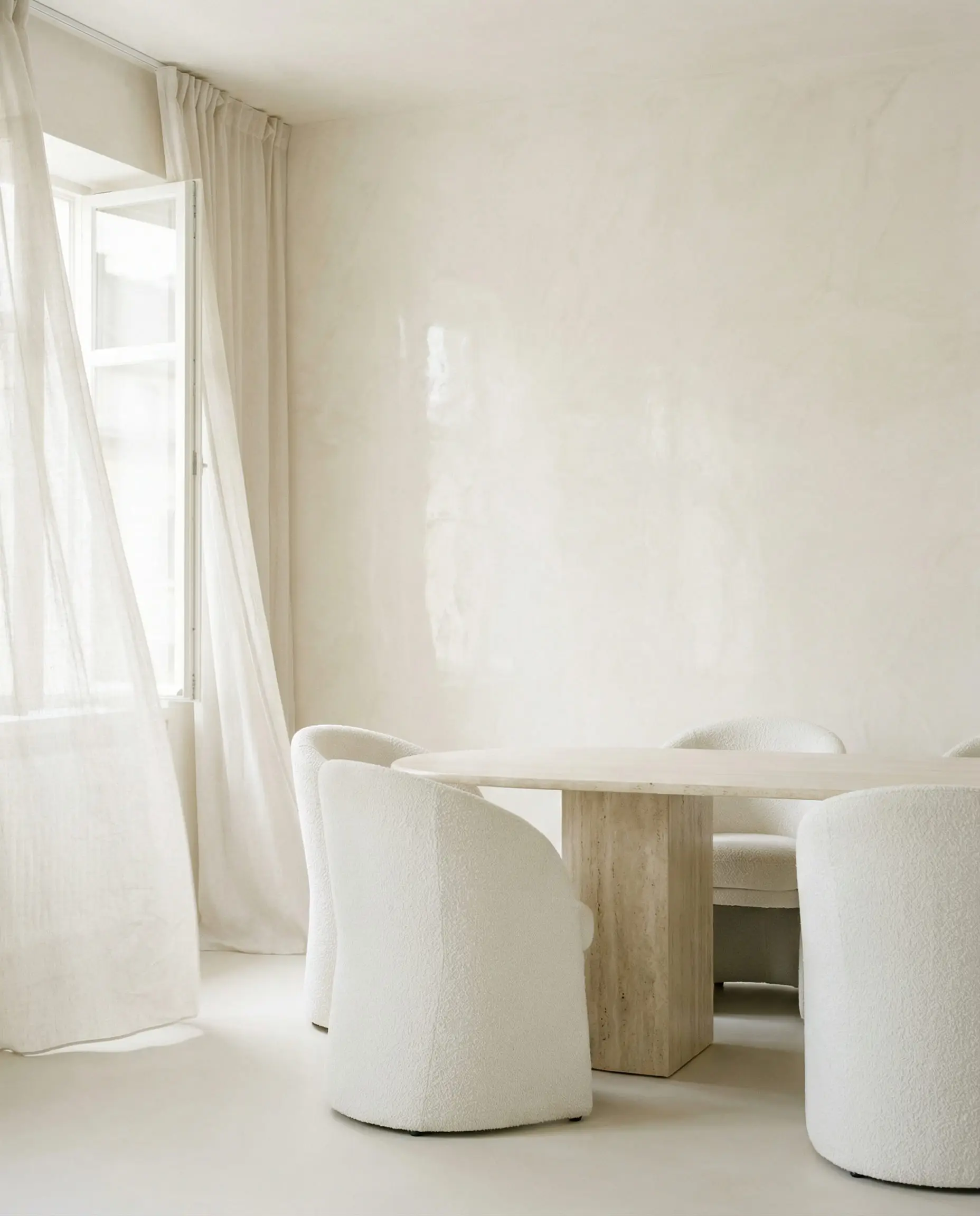 Serene minimalist dining room with creamy beige Venetian plaster walls, a travertine table, and white bouclé chairs.