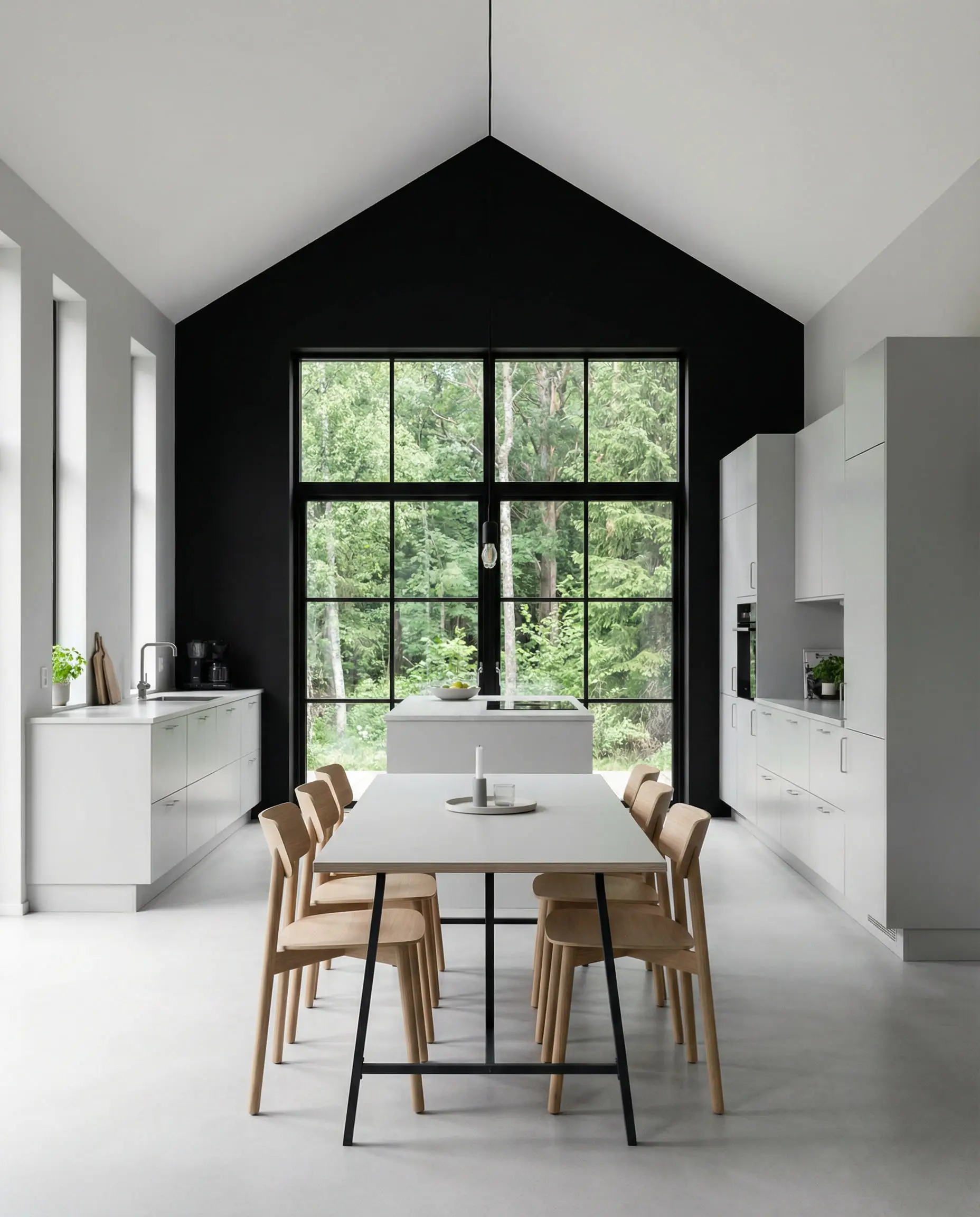 Modern light gray kitchen featuring a single matte black accent wall framing a view of a green forest.