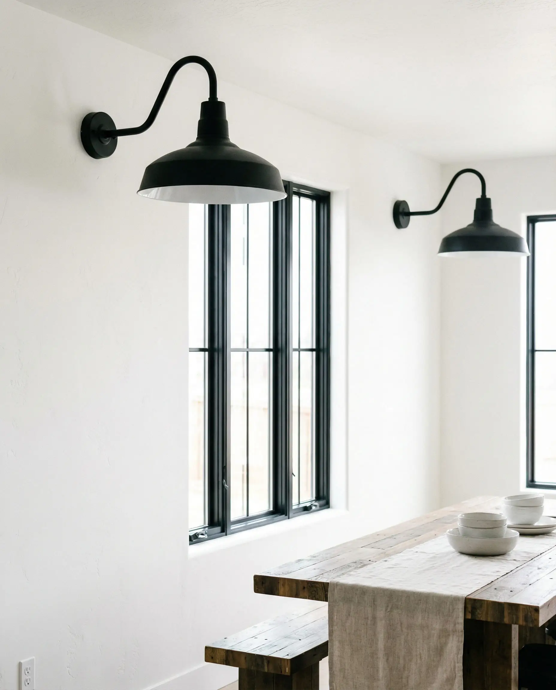 White dining wall featuring two large matte black gooseneck barn sconces flanking a window.