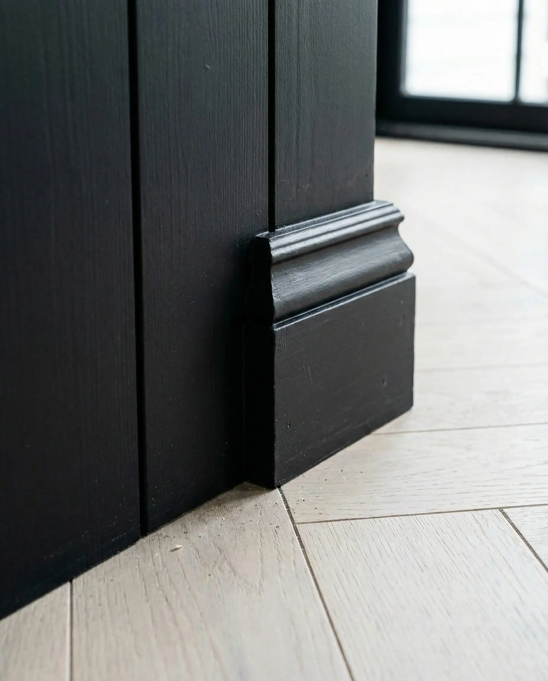 Floor level detail showing black baseboards matching the vertical black shiplap wall seamlessly.