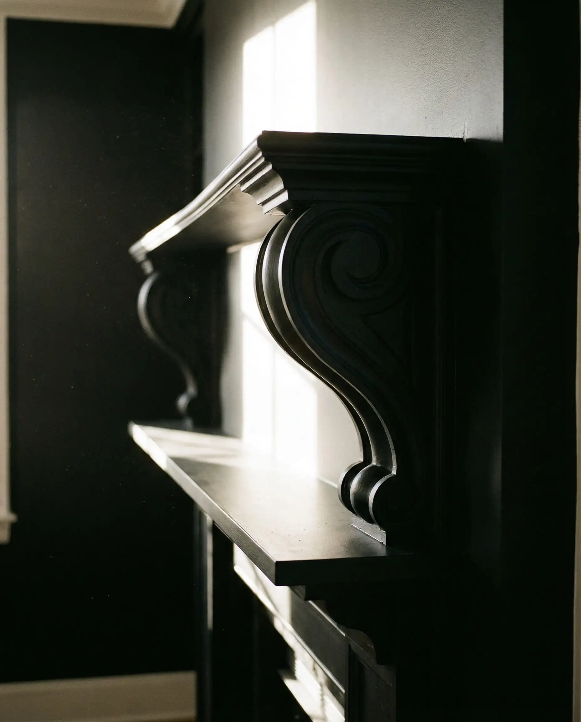 Profile silhouette of chunky wooden corbels supporting a mantel, all painted black.