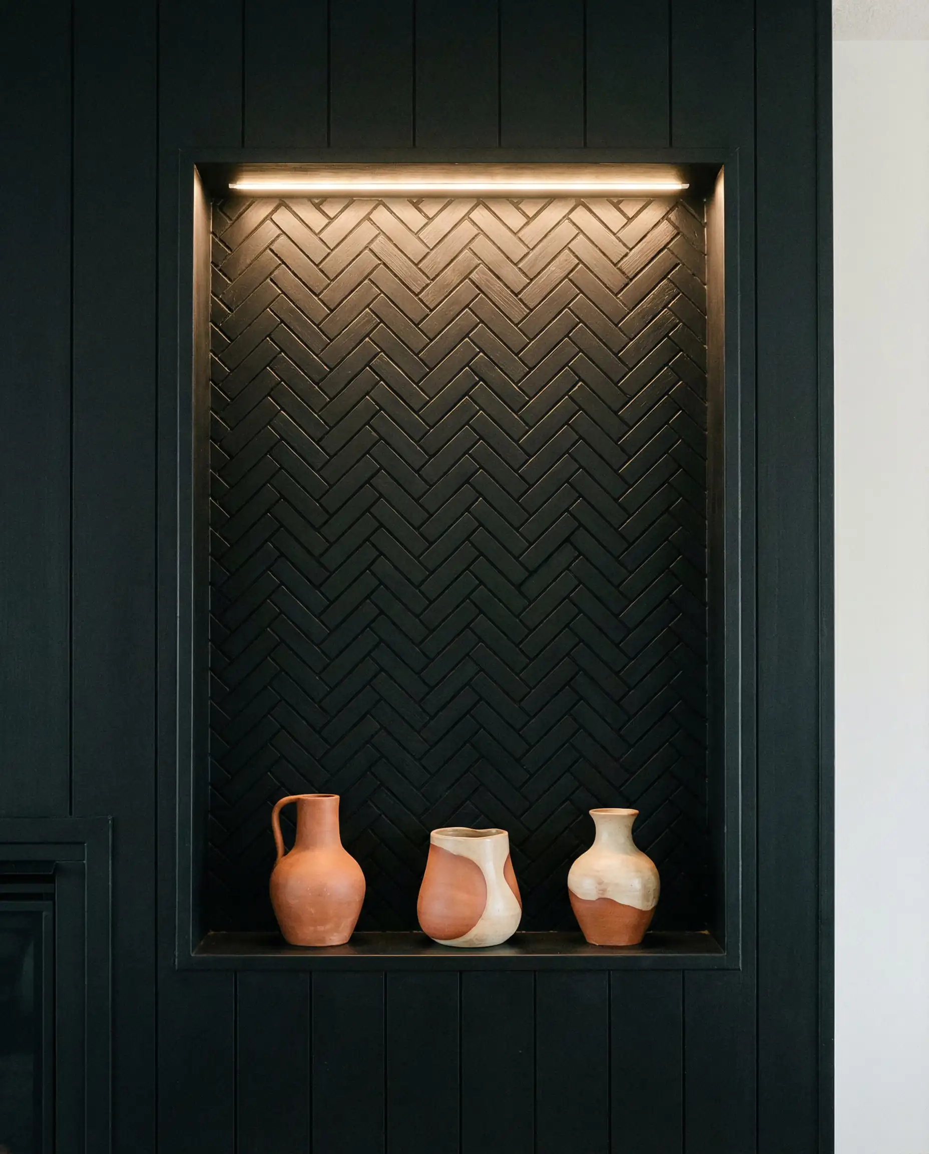 Recessed niche above a fireplace featuring an intricate black herringbone wood pattern back panel.