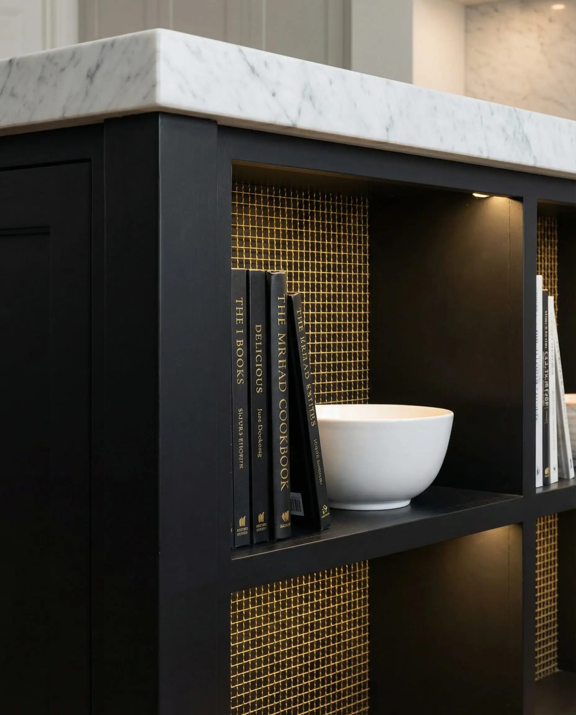 Detail of black kitchen island end-cap featuring open storage with gold wire mesh backing and cookbooks.