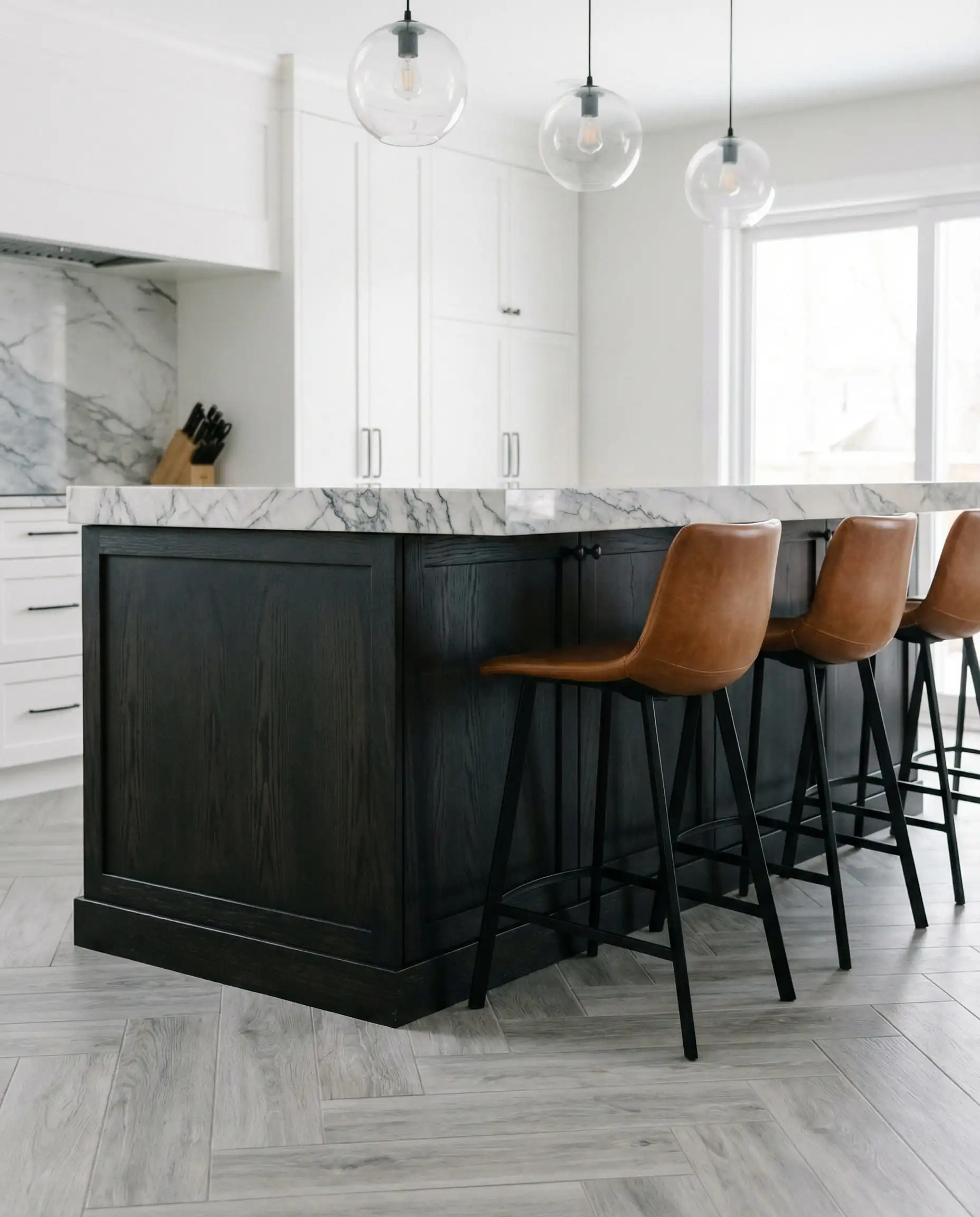Vertical shot of a black stained wood kitchen island on a light gray chevron wood floor.