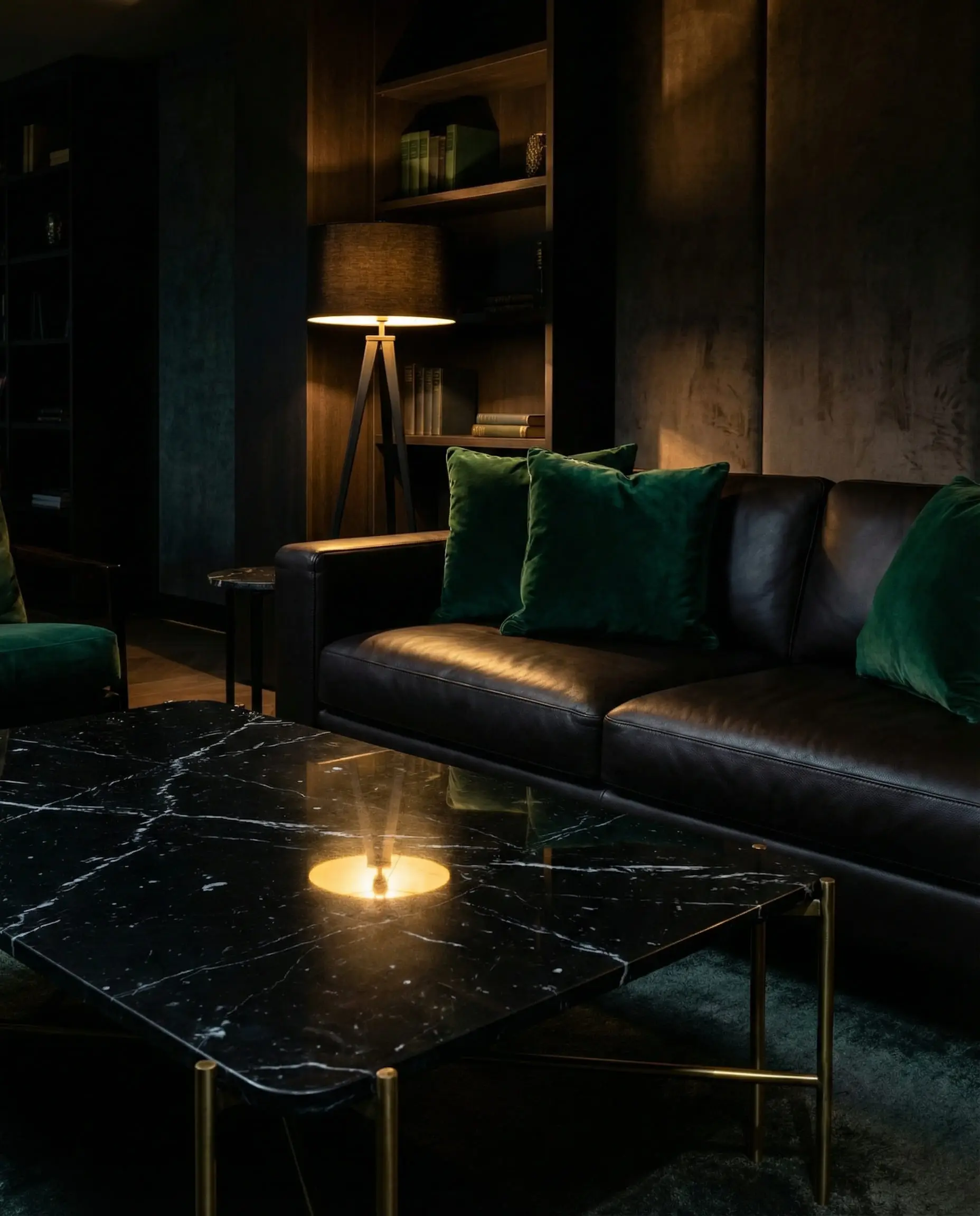 Moody interior shot of a black Nero Marquina marble table with white veins paired with a dark espresso leather sofa and velvet pillows.