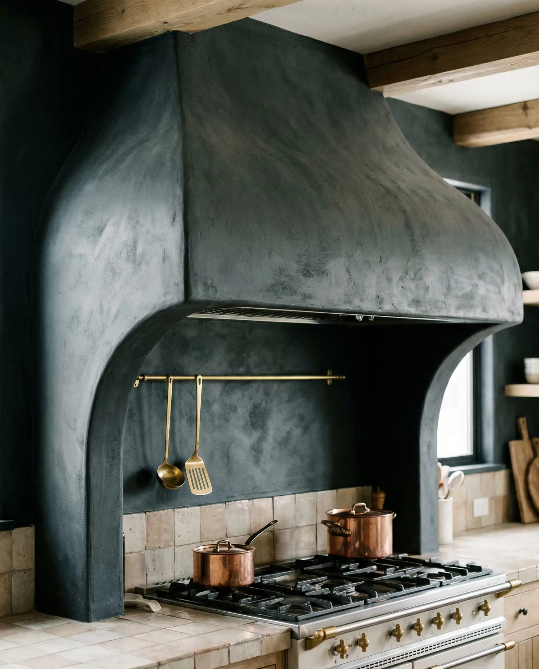 Curved black plaster range hood with a thin gold utensil rail running along the bottom lip.