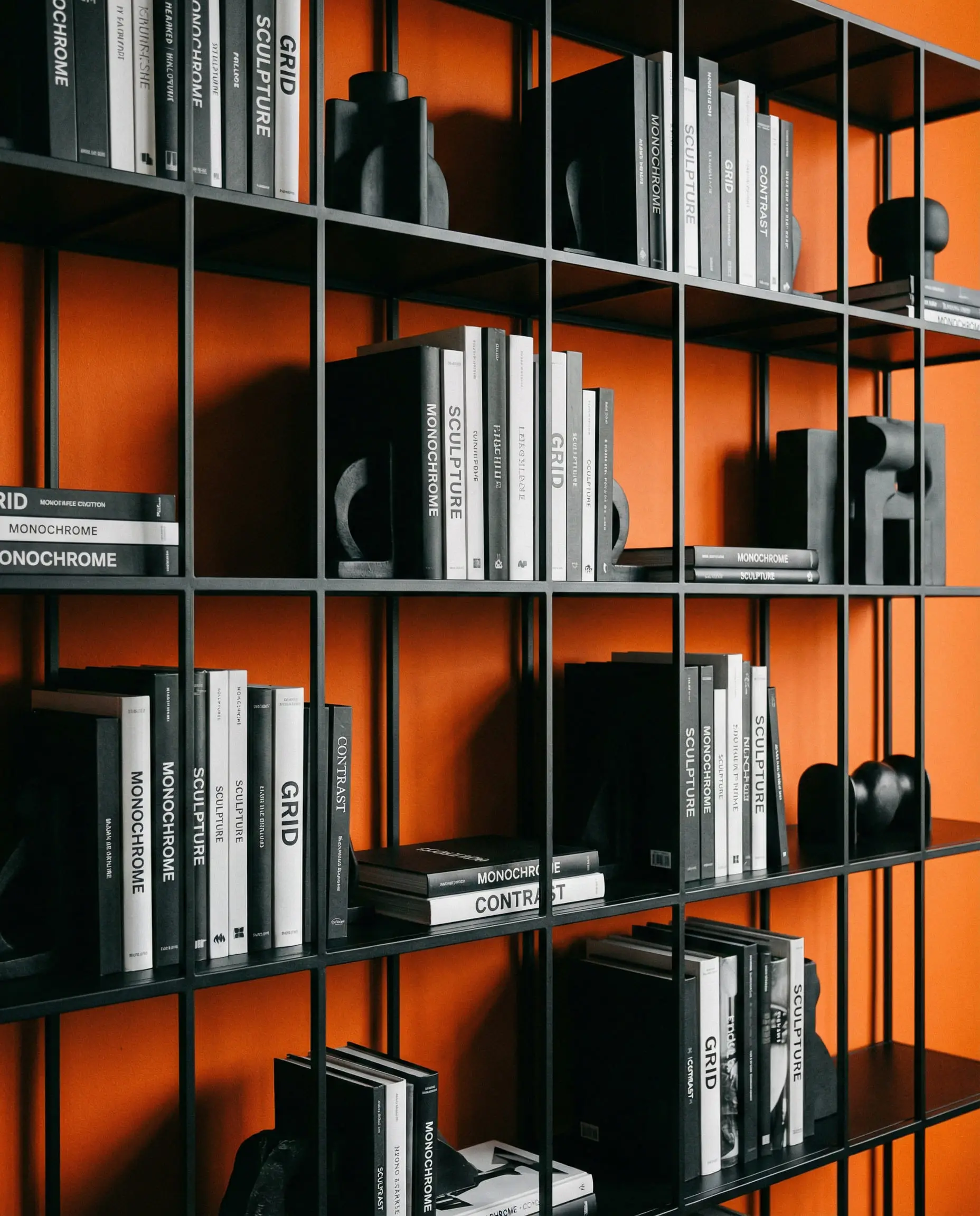 Matte black metal shelving unit styled with monochrome black and white books against a vibrant orange wall.