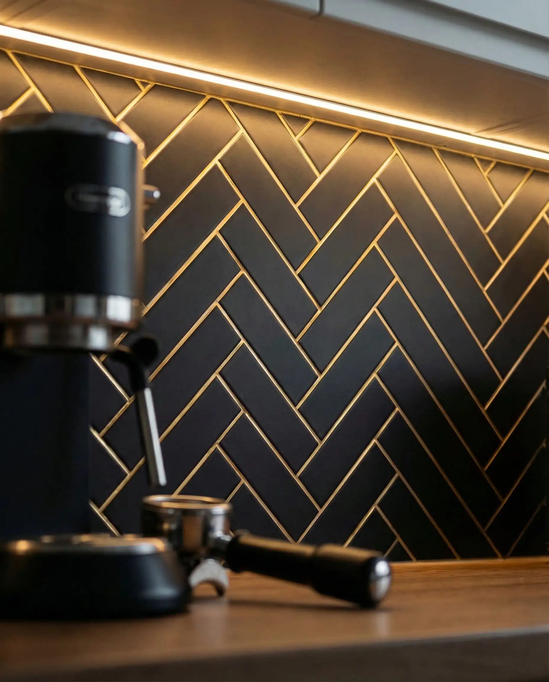 Matte black subway tile backsplash featuring metallic gold grout in a herringbone pattern.
