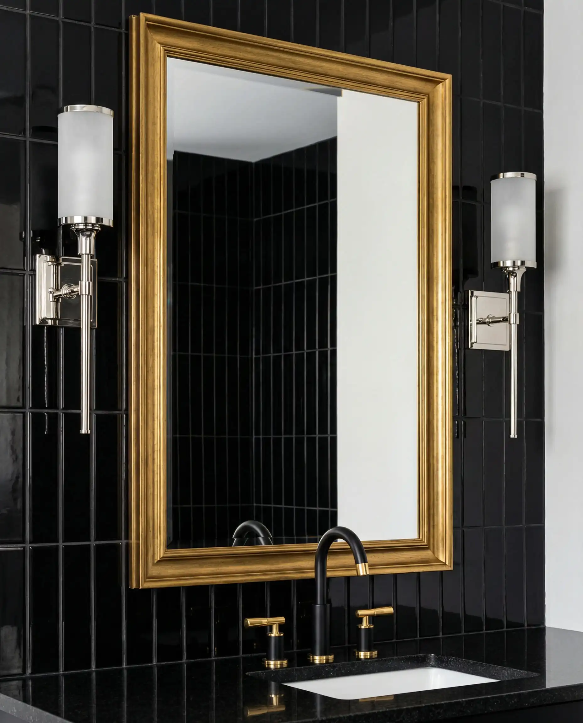 Bathroom vanity with black subway tile, gold mirror frame, and chrome wall sconces.