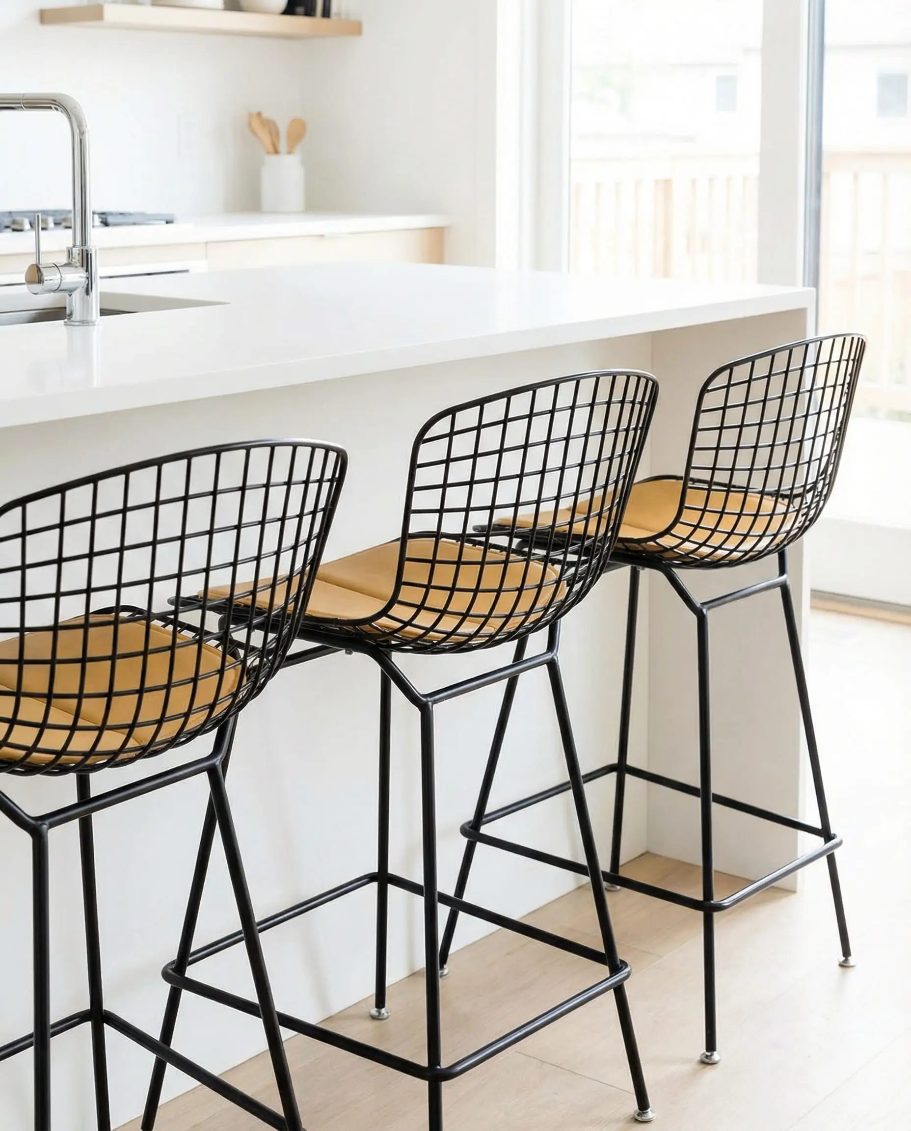 Modern black wire bar stools with tan leather seat pads at a white island.