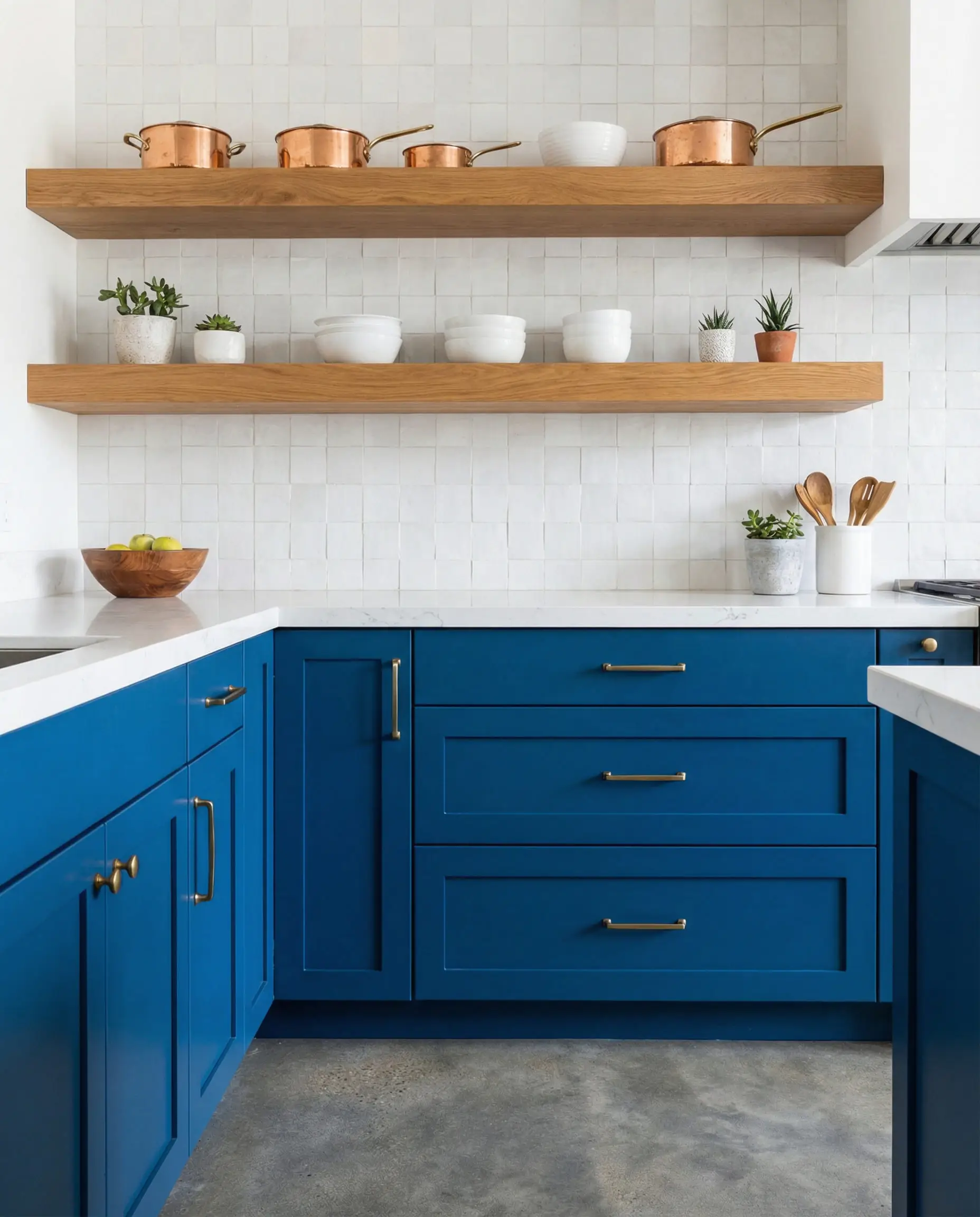 Deep blue lower cabinets with floating wood shelves on a white tiled wall, grounded by gray concrete floors.