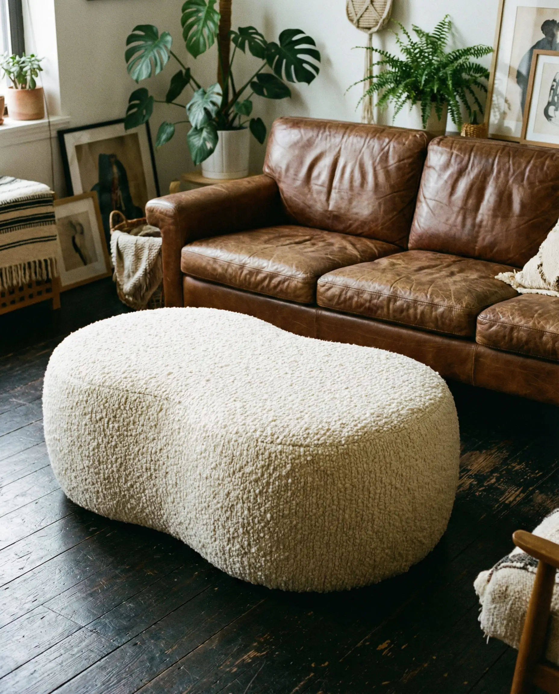 Curved creamy white boucle fabric ottoman serving as a coffee table in front of a vintage worn brown leather couch.