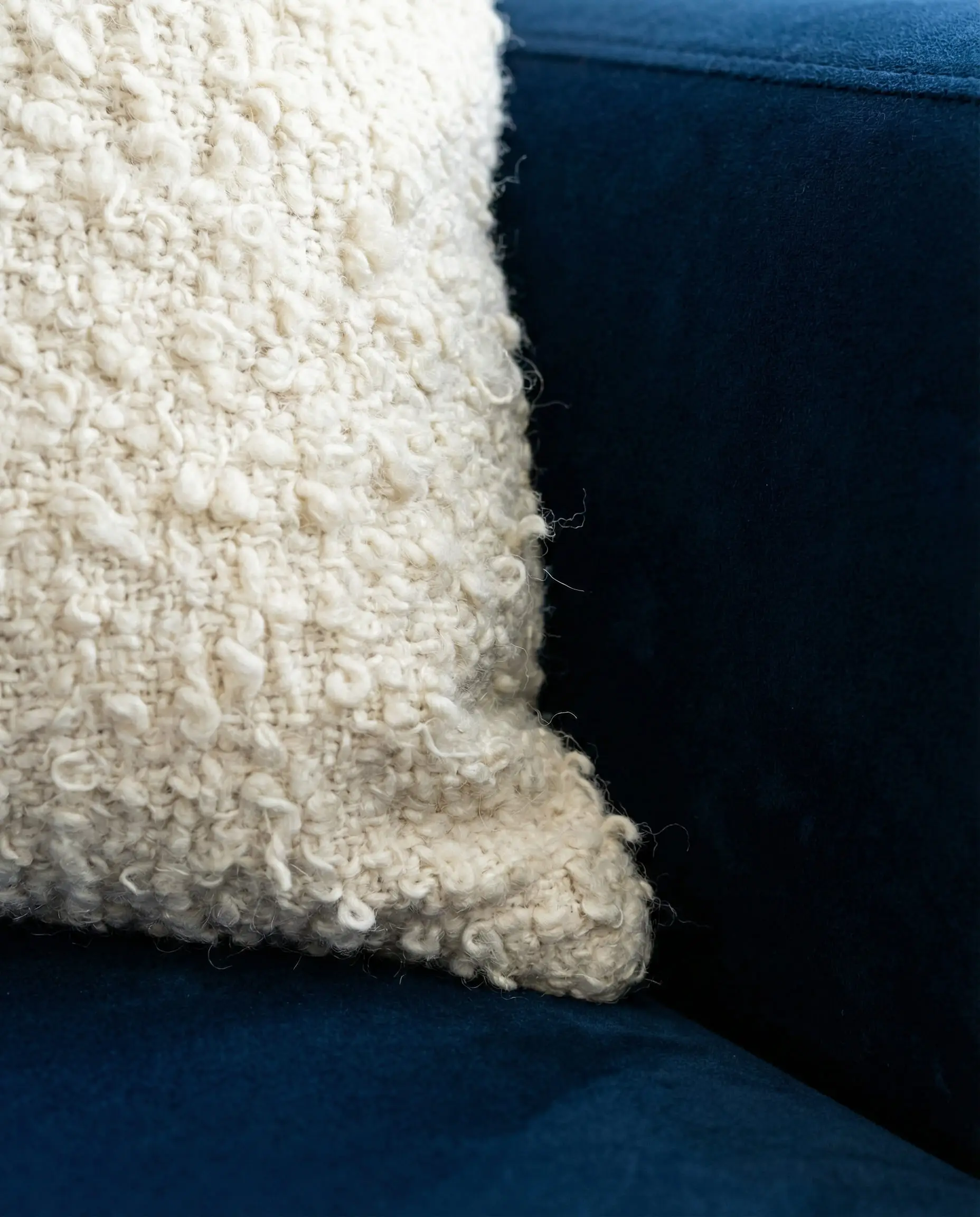 Extreme close-up of creamy white bouclé fabric texture pressing against smooth navy blue velvet.