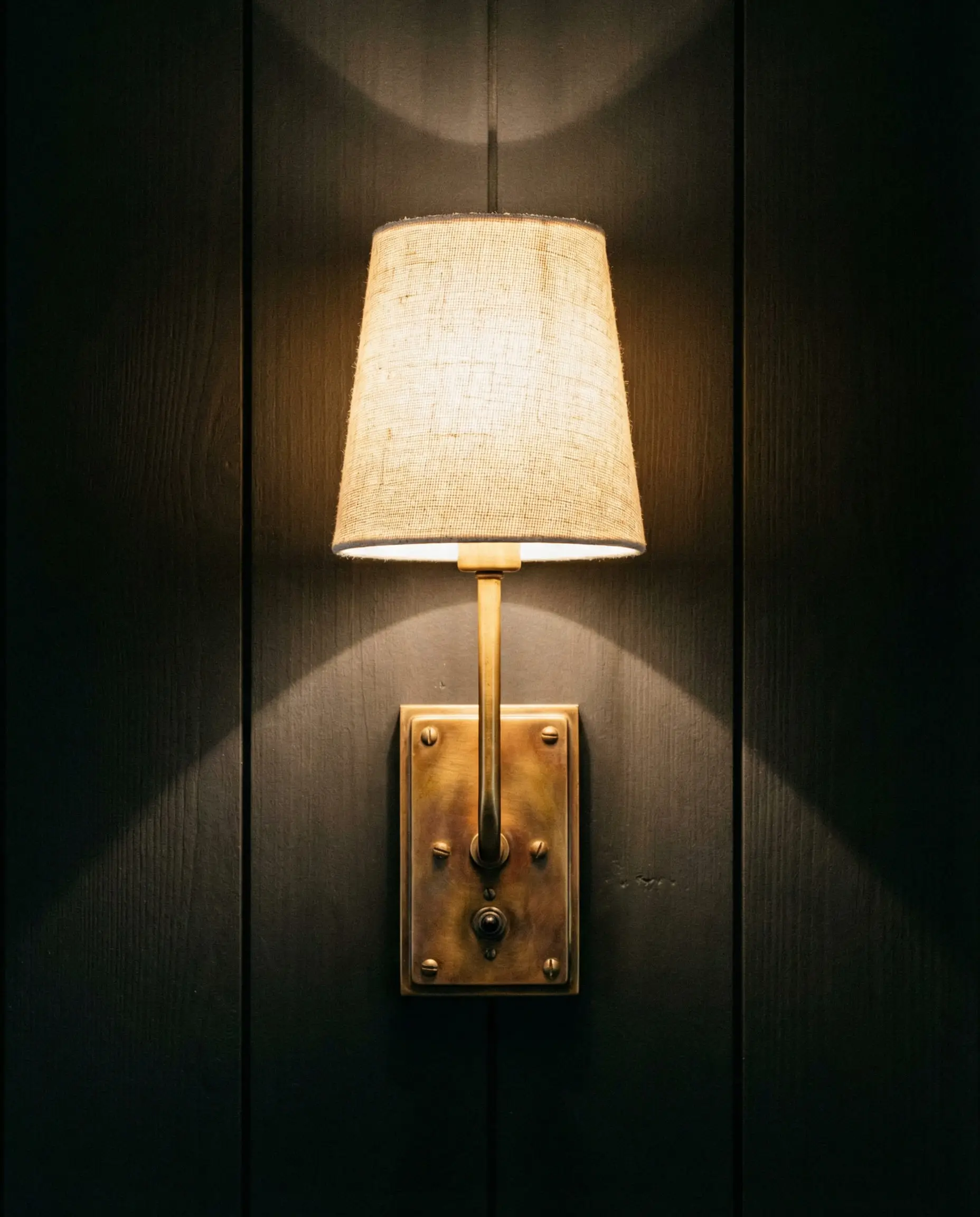 Detail of unlacquered brass wall sconce mounted on vertical matte black shiplap.
