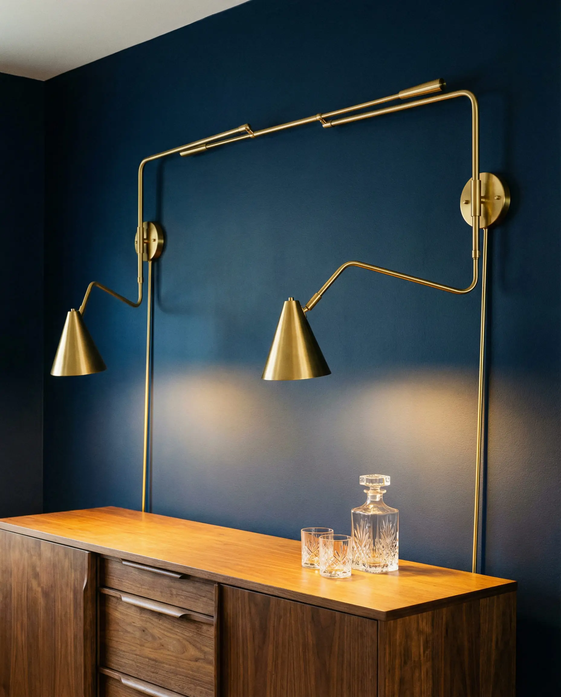 Navy blue dining wall featuring two articulated brass swing-arm sconces extending over a walnut sideboard.