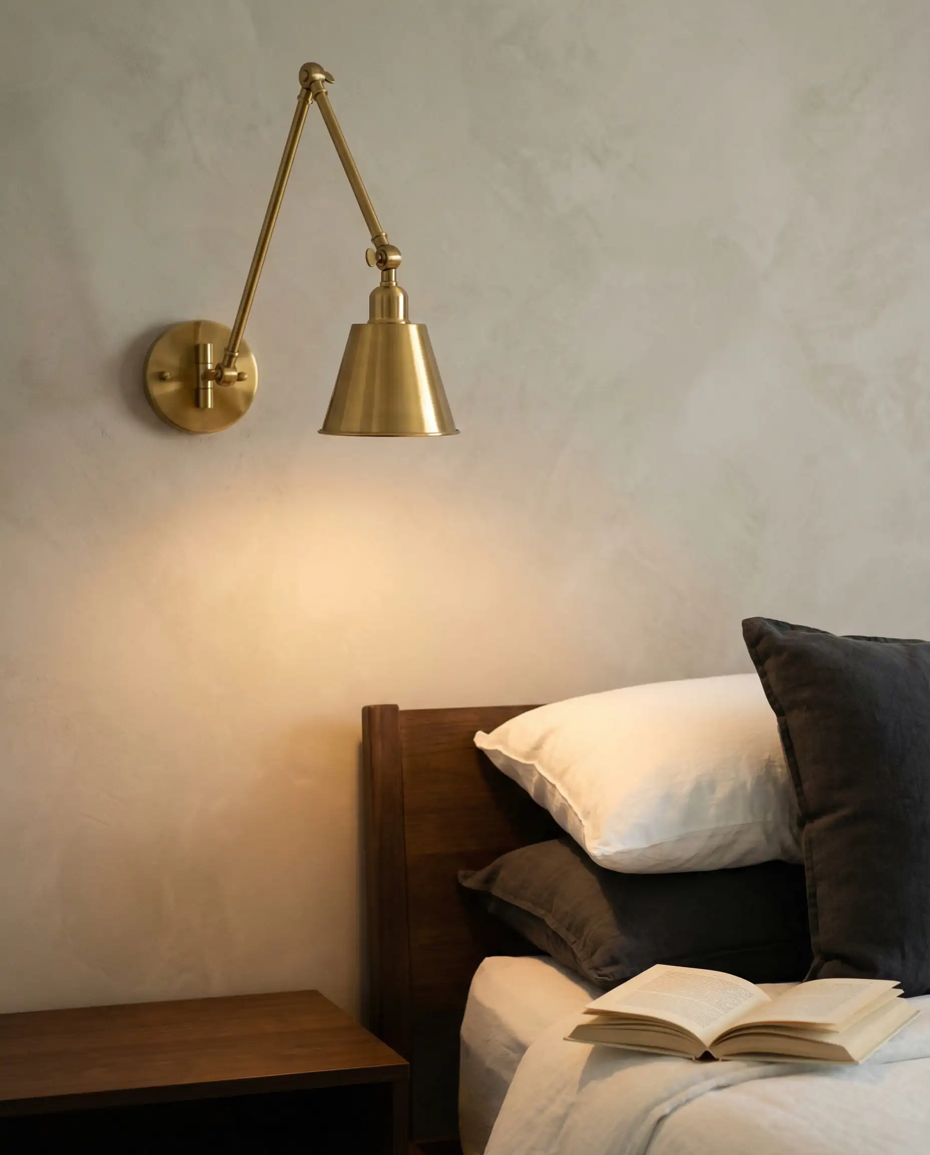 Articulating brass wall sconce mounted above the bed freeing up nightstand surface area.