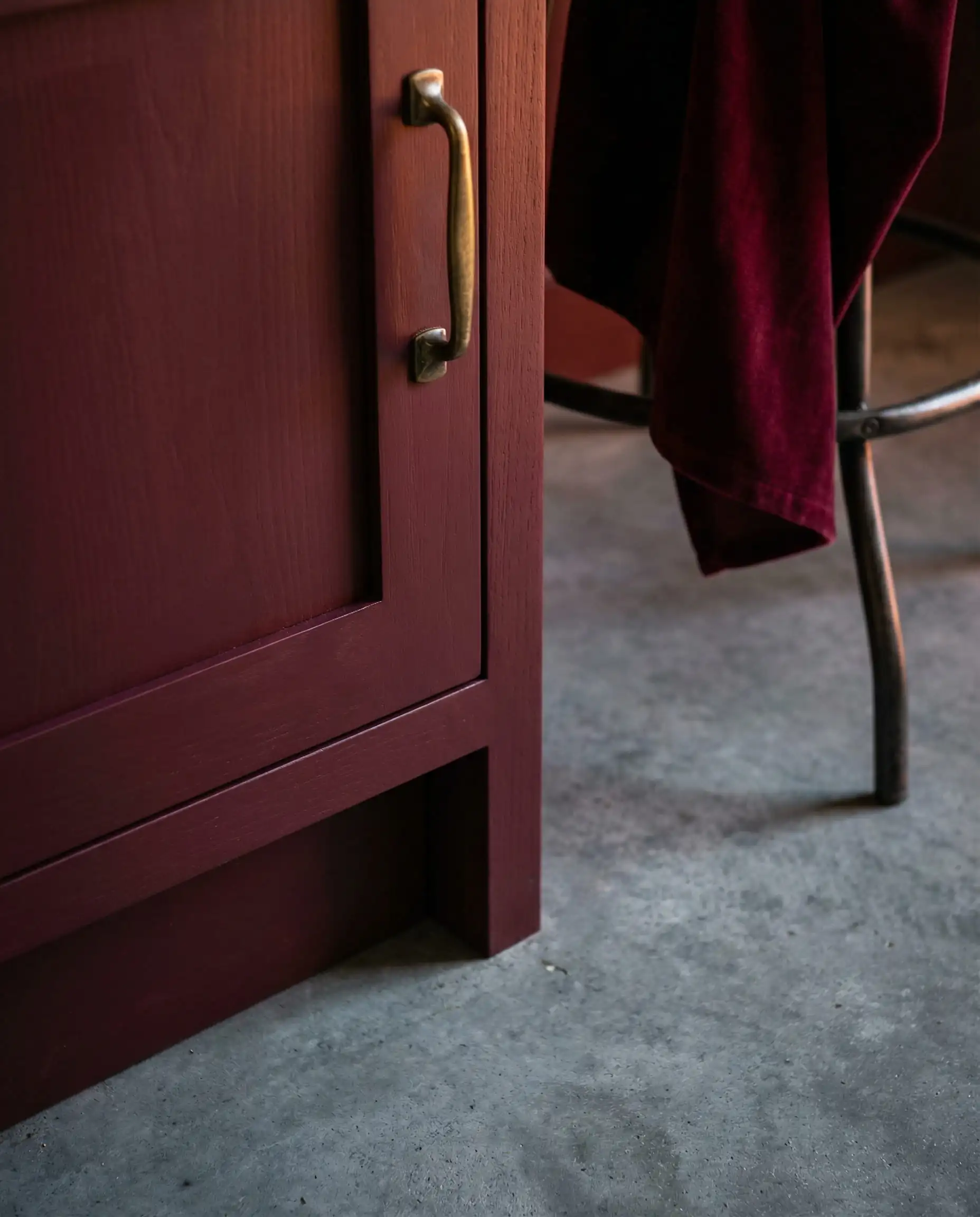 Detail of burgundy/merlot cabinet paint color next to a cool industrial gray concrete floor.