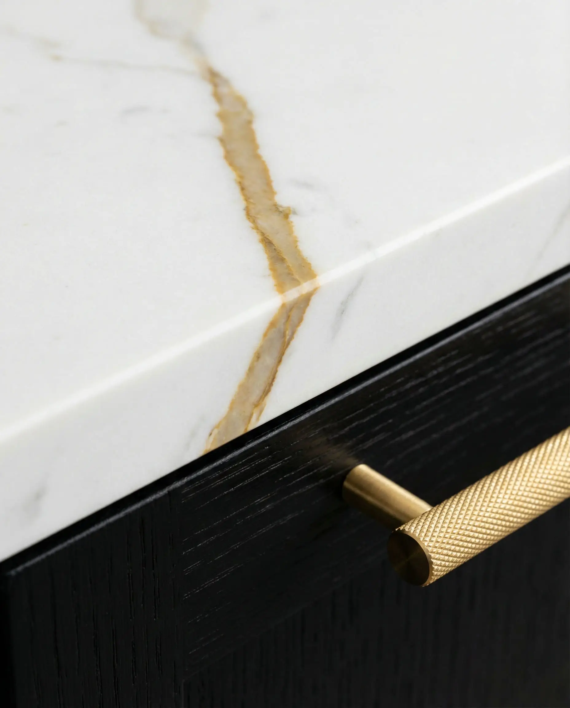 Close-up of Calacatta marble edge showing a gold vein matching the brass cabinet hardware on black drawers.