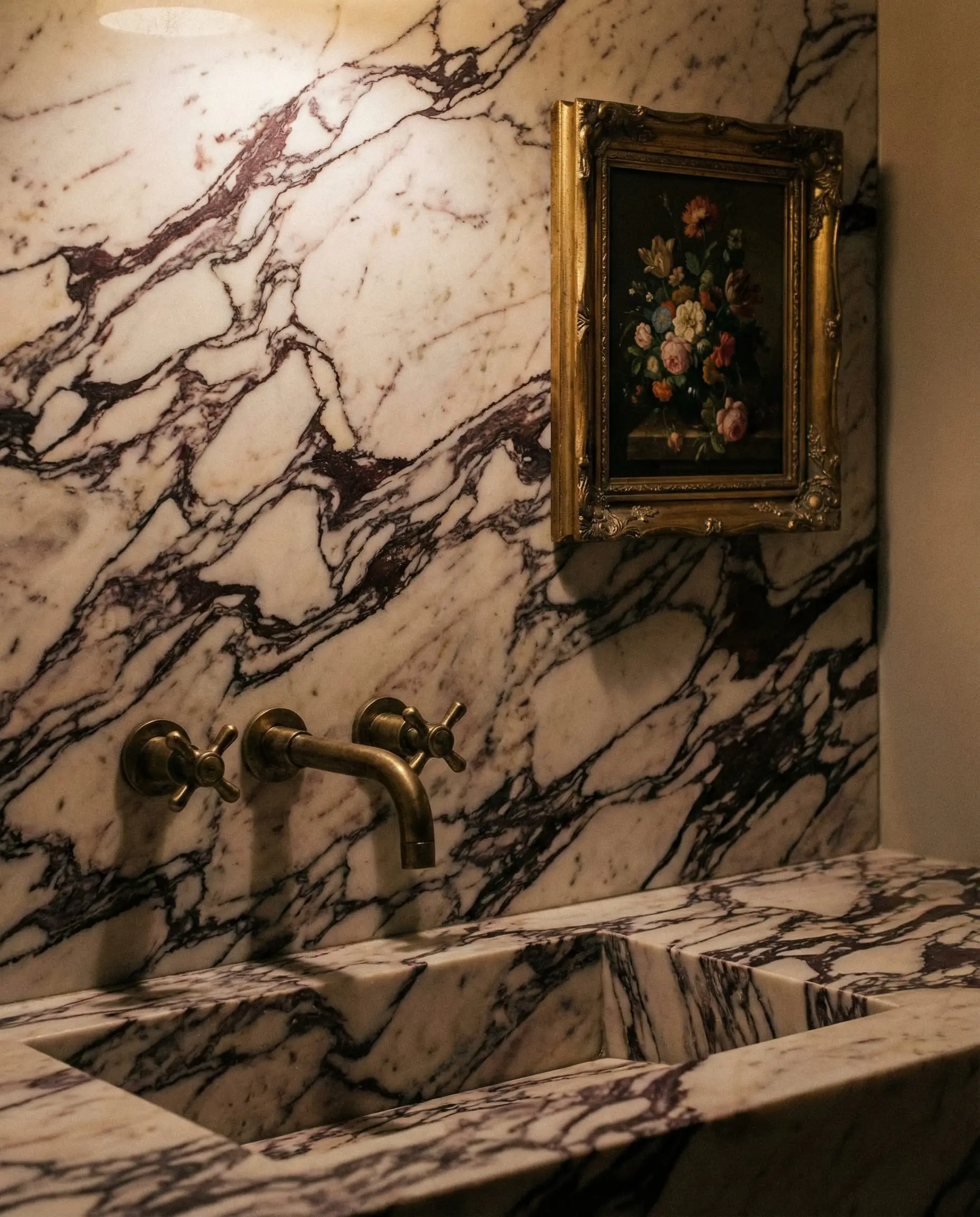 Powder room vanity featuring a statement slab of Calacatta Viola marble with unlacquered brass wall-mount faucets.