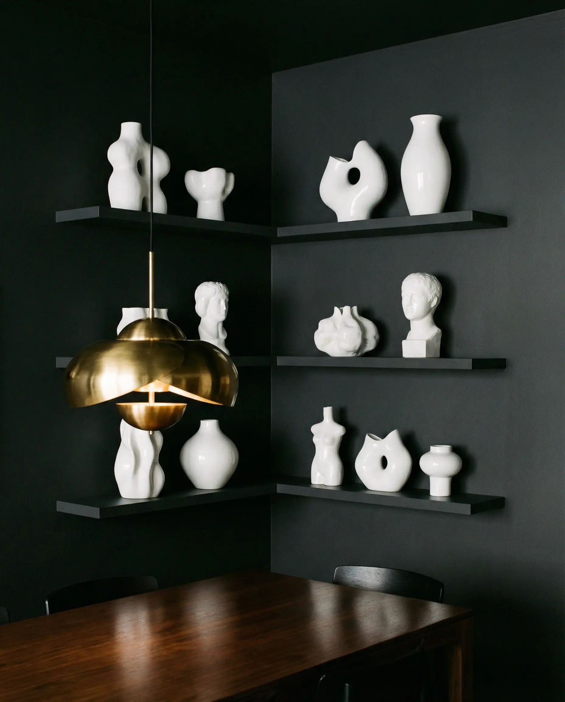 Moody charcoal grey dining wall with matching dark shelves holding stark white porcelain vases.
