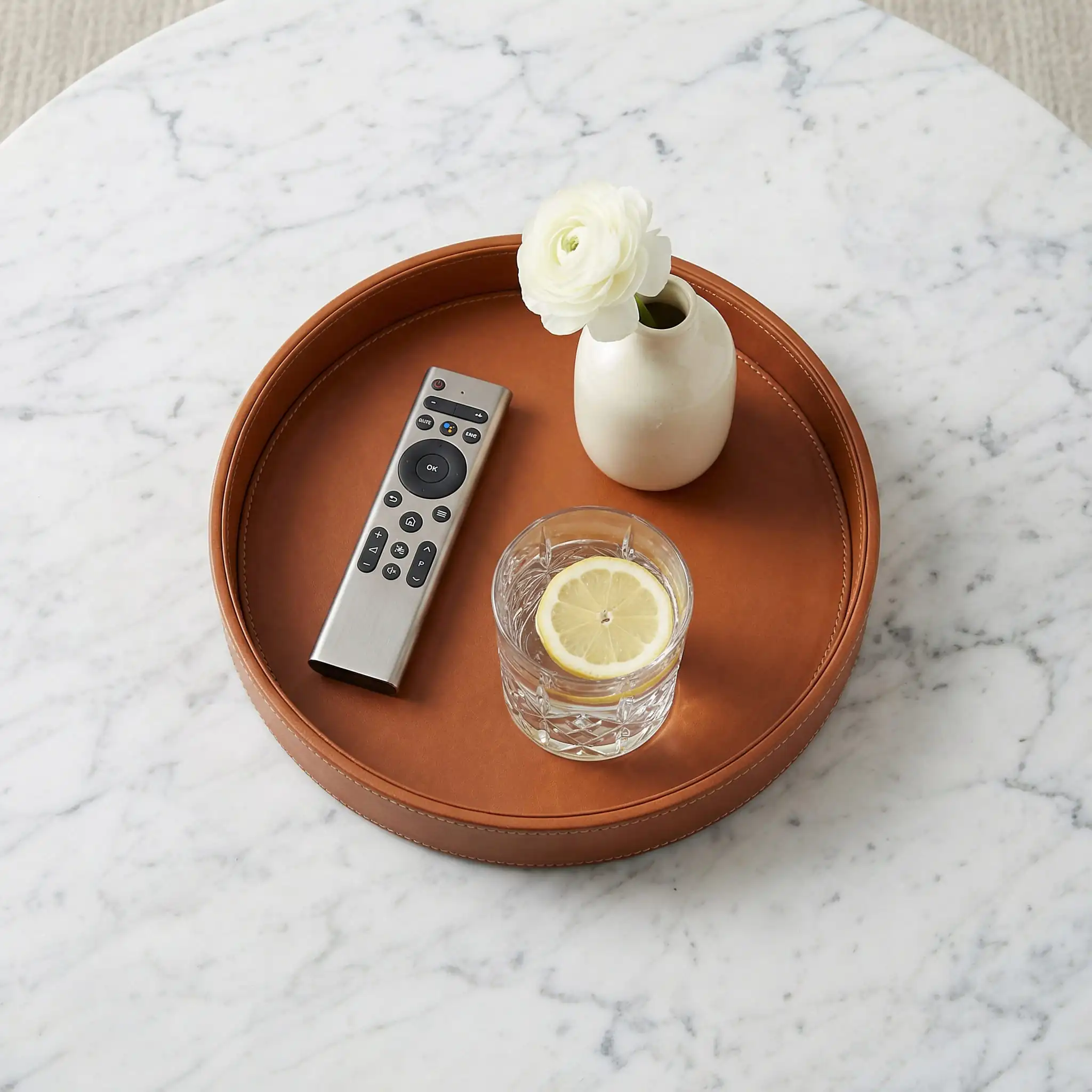 Overhead flat lay shot of a leather tray organizing remotes and coasters on a marble table.