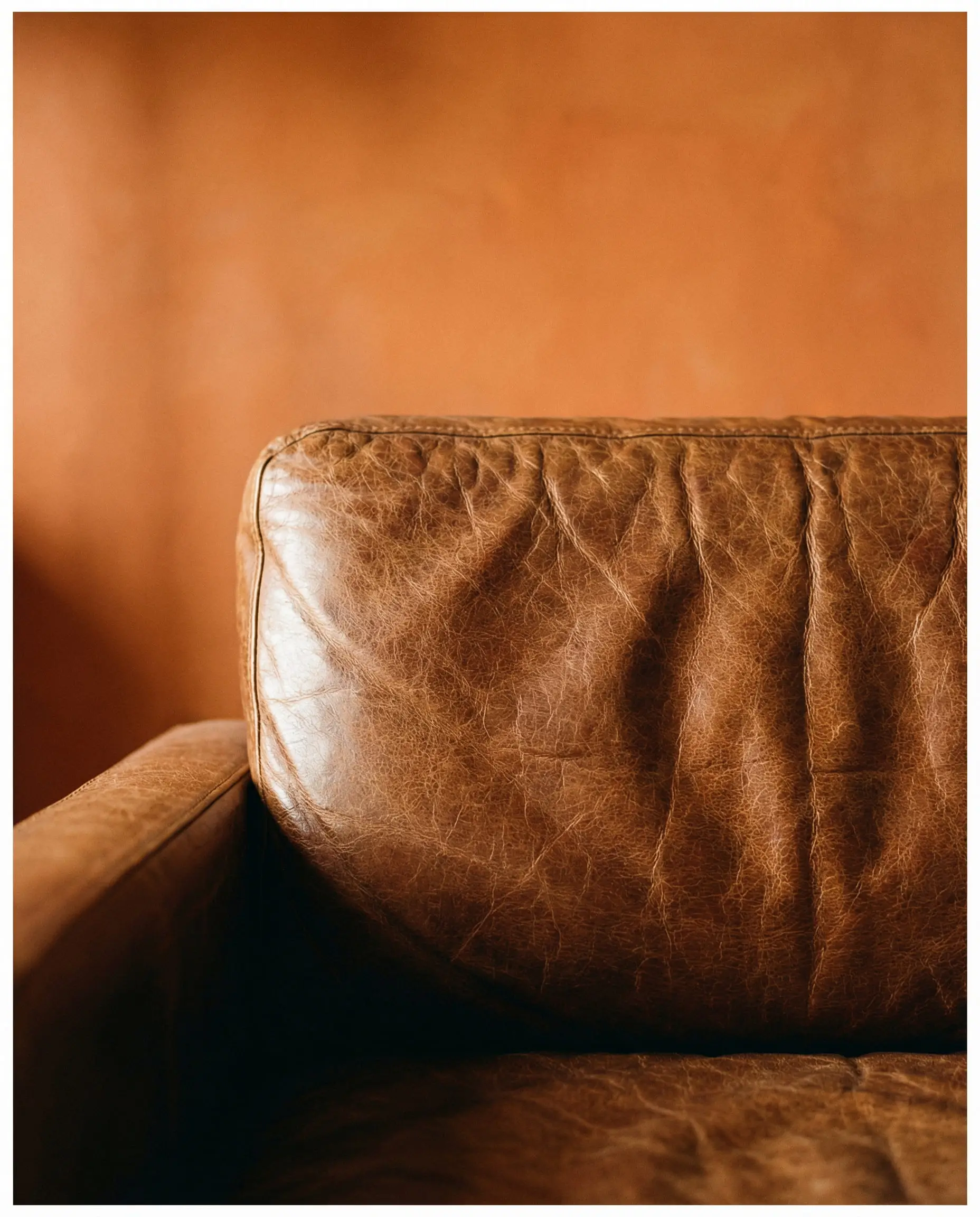 Close-up detail of cognac brown leather sofa texture against a terracotta wall background.