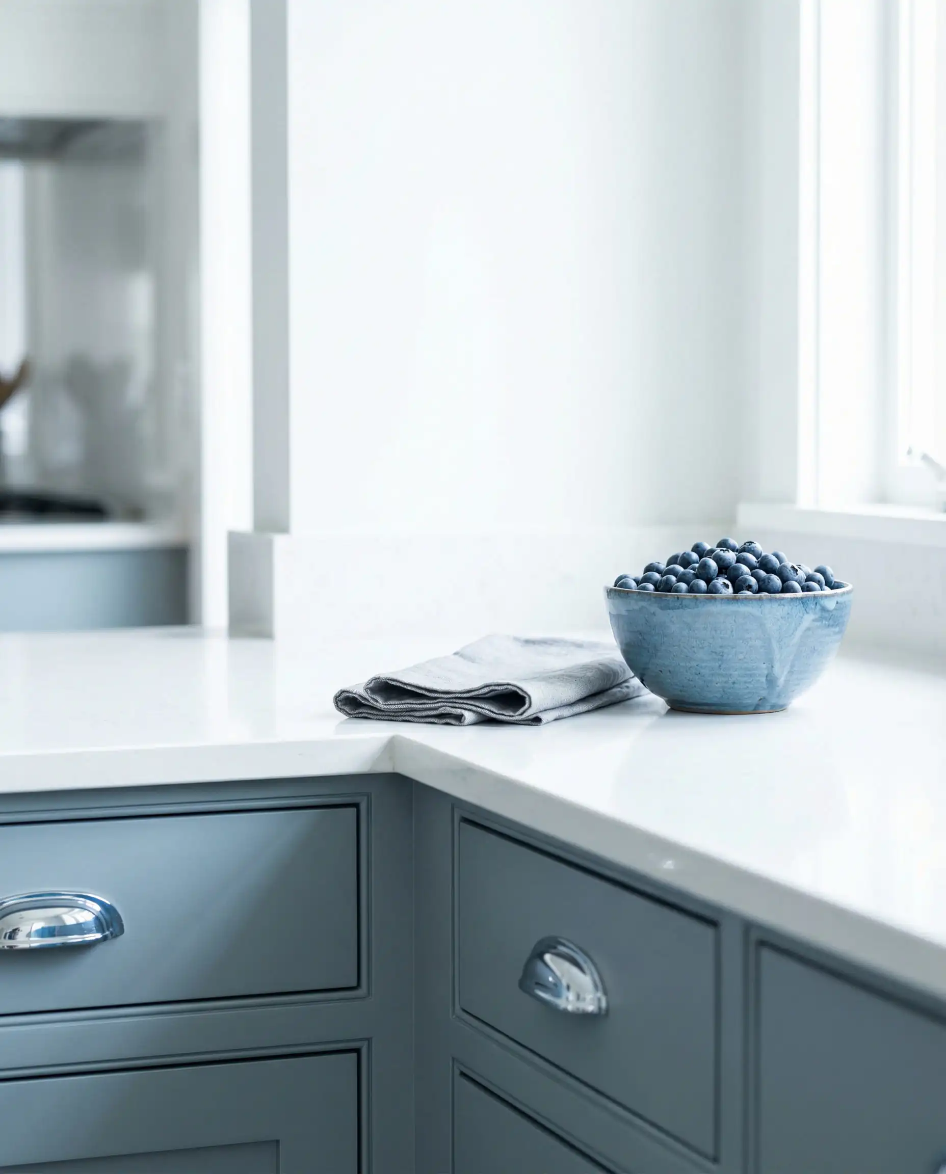 Close-up of coastal-style blue-gray kitchen cabinets paired with bright white quartz countertops and polished nickel hardware.